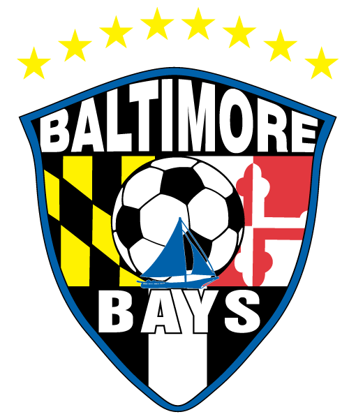 BBAY6 - Baltimore Bays "Crest Transfer" - POCKET Color. This shield-shaped crest features a blue border with "BALTIMORE" in white at the top and "BAYS" at the bottom. The center background displays the yellow-and-black and red-and-white patterns of the Maryland state flag behind a black-and-white soccer ball. A blue sailboat silhouette is superimposed over the lower half of the soccer ball. Above the shield is an arc of eight yellow stars.