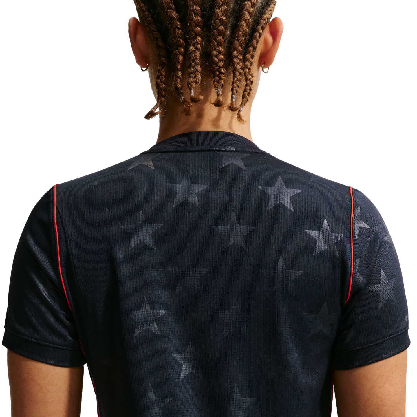 Back view of a person with brown braided hair wearing a navy blue shirt with a grey star pattern and red trim on the sleeves, against a black background.
