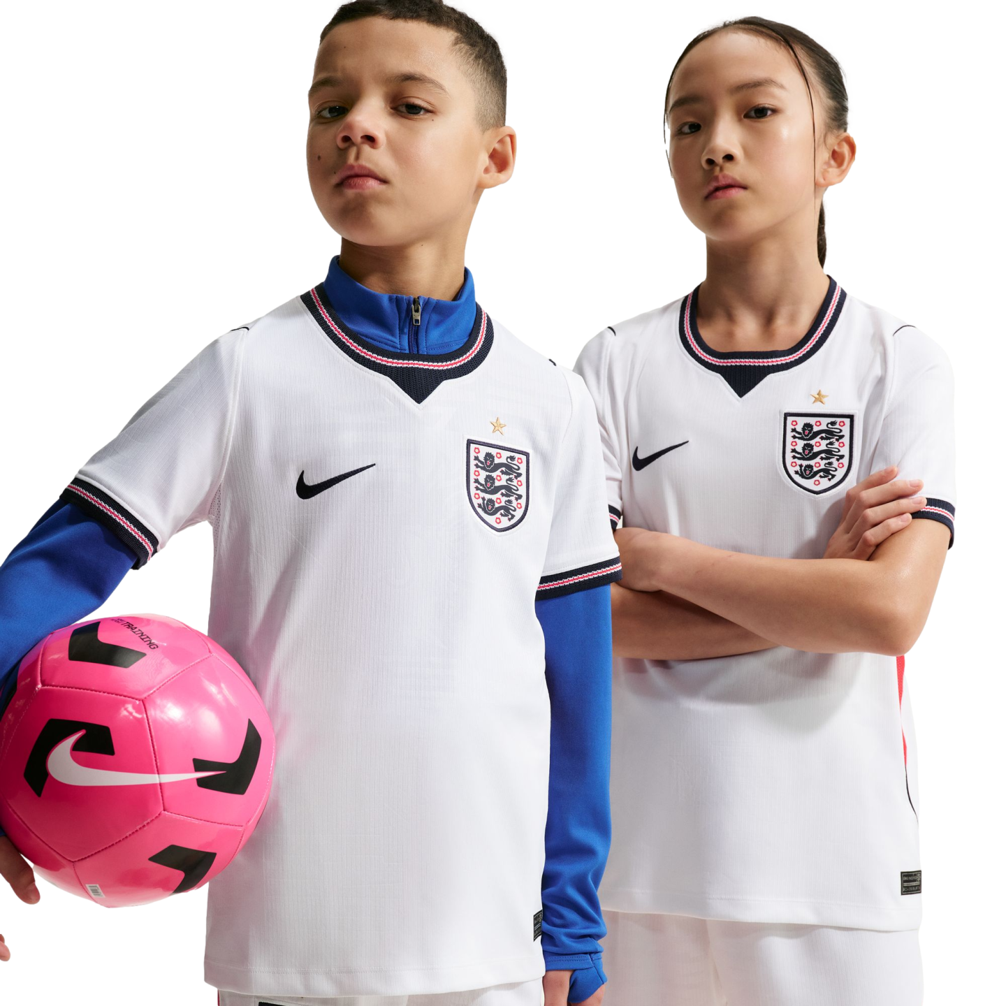 Two children pose in white England national team football kits against a black background. The boy holds a pink football.