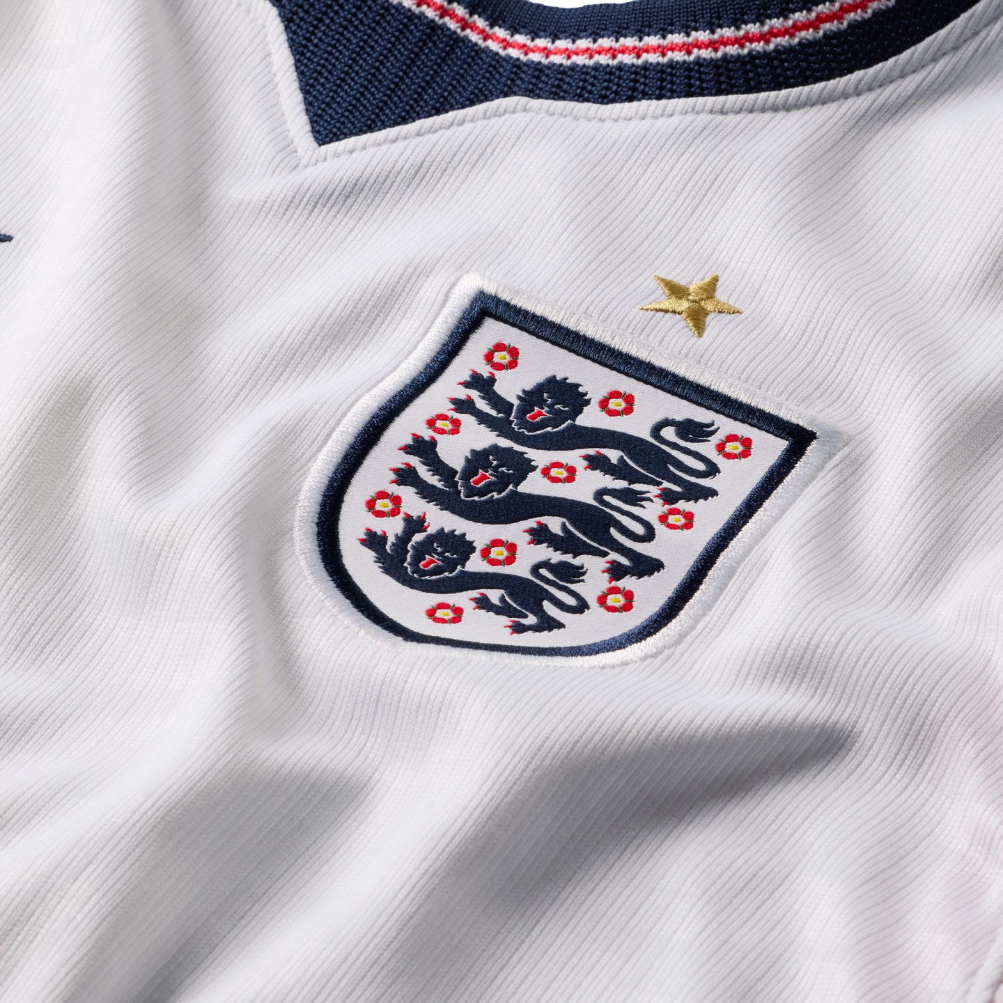 Close-up of the England national football team crest on a white jersey, showing the Three Lions, a gold star above, and a navy, red, and white collar at the top.