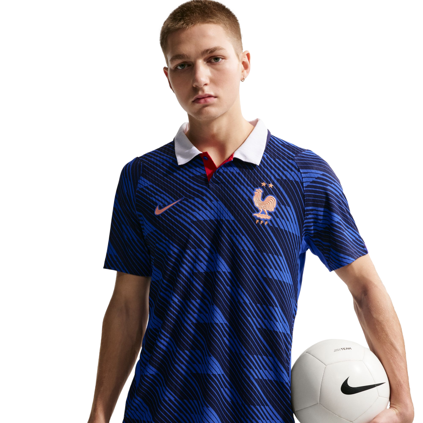 A man wearing a blue Nike France national team soccer jersey with a white collar, holding a white soccer ball against a black background.