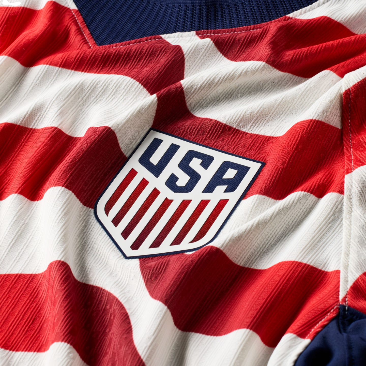 Close-up of a textured red and white striped USA soccer jersey with the official team shield crest in the center.