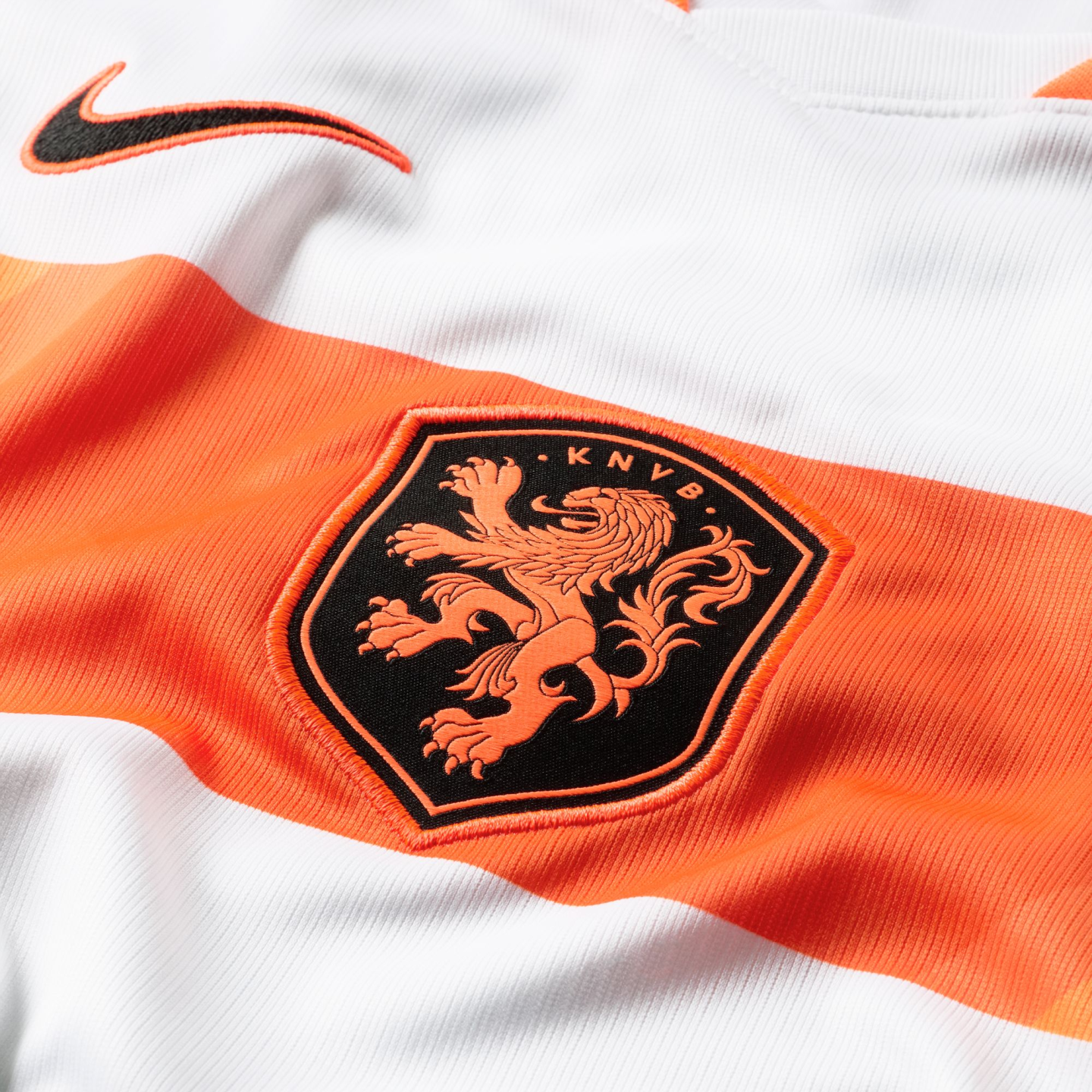 A close-up of a white and orange Netherlands soccer jersey featuring the black and orange Nike swoosh logo above the KNVB crest, which depicts an orange rampant lion on a black shield.