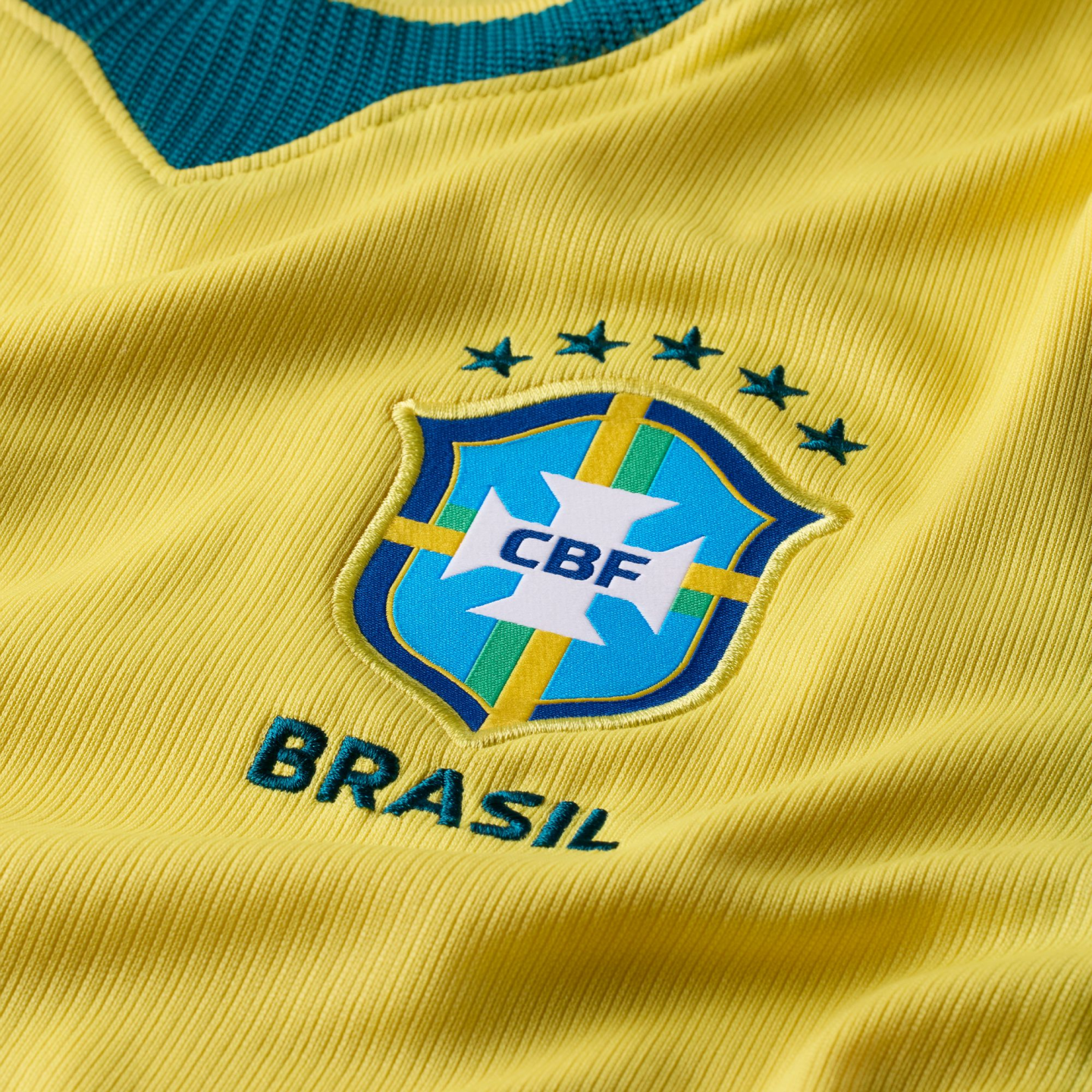 Close-up of the yellow Brazil football jersey's CBF crest, with five green stars above and "BRASIL" embroidered below.
