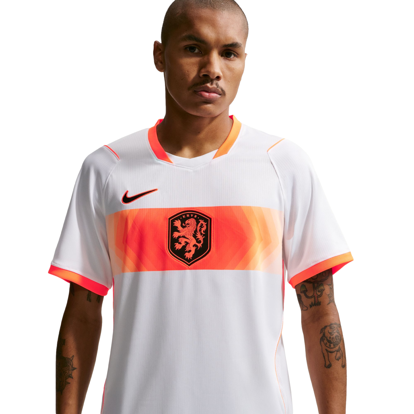 A waist-up portrait of a man wearing a white Netherlands national football team away jersey. The jersey features a wide orange band across the chest with a central lion crest and a black Nike logo on the right. The man has short-cropped hair, a mustache, and tattoos on his forearms, set against a solid black background.