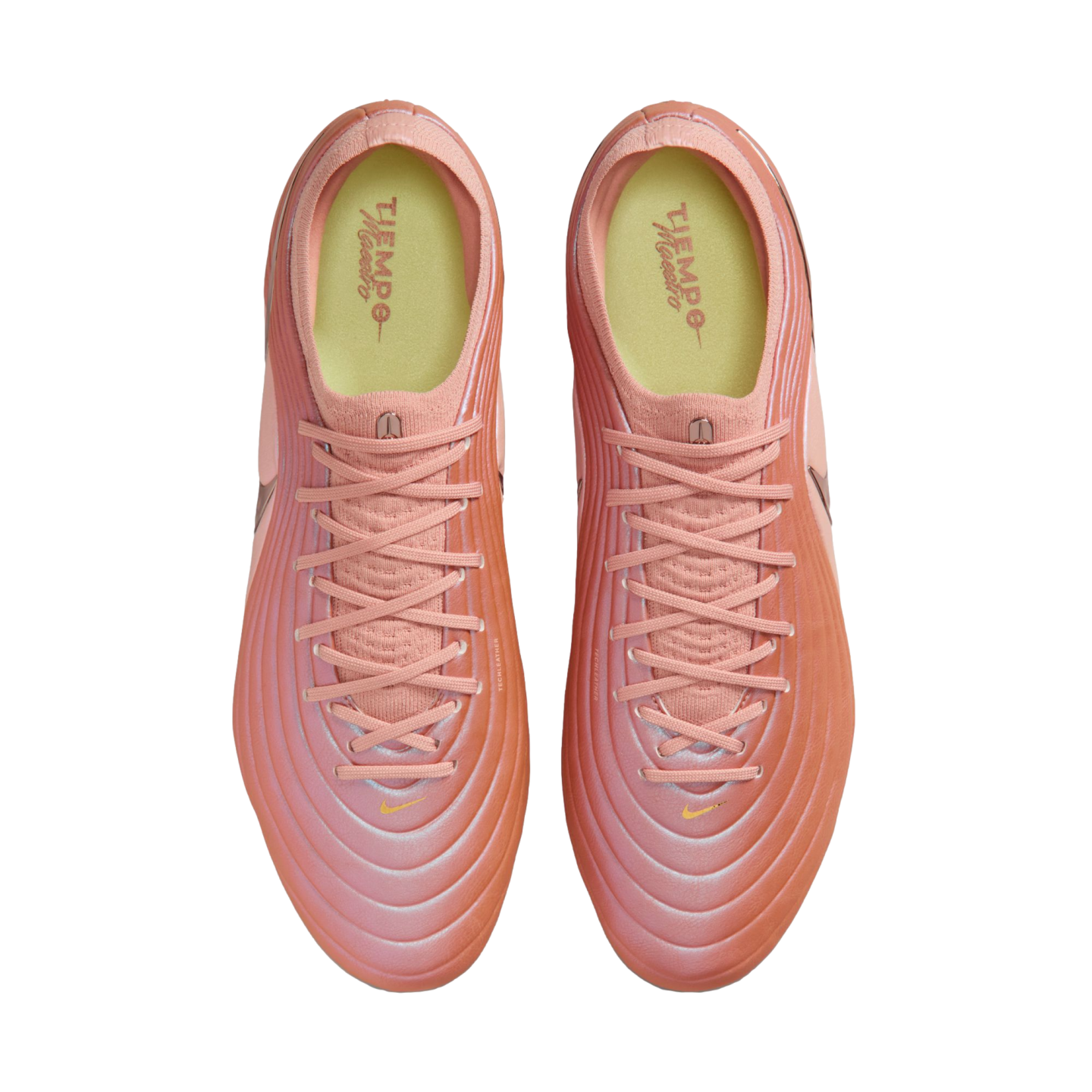 Top-down view of a pair of pinkish-orange Nike soccer cleats with a textured upper and yellow insoles.