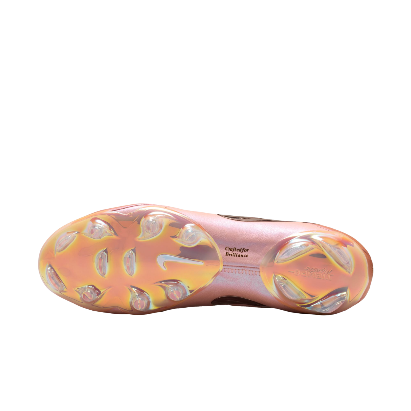 Bottom view of an iridescent pink and gold Nike Tiempo soccer cleat sole plate with clear studs and the text "Crafted for Brilliance" against a black background.