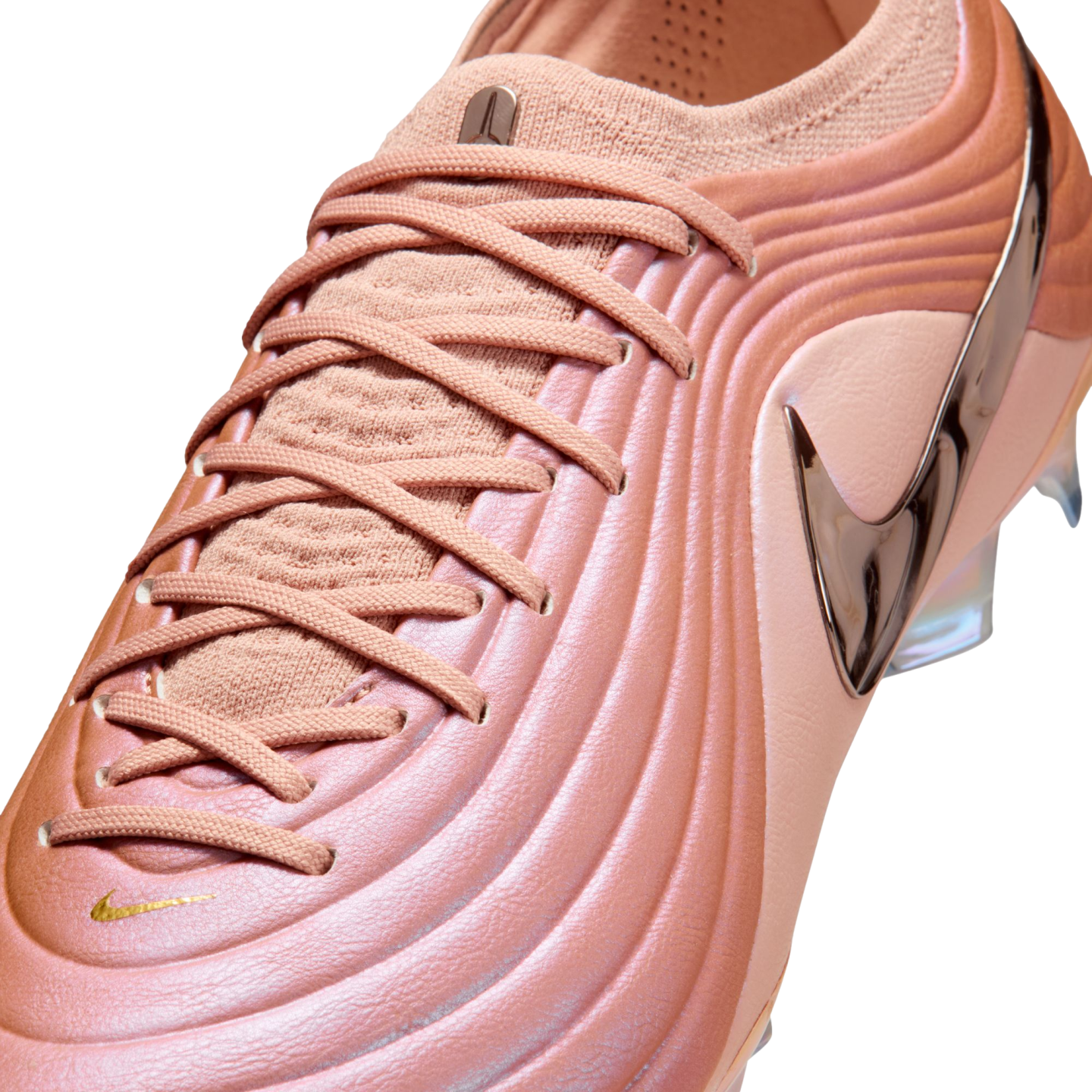 Close-up of a rose gold Nike soccer cleat with a ridged, metallic upper, matching laces, and a large bronze Nike swoosh.
