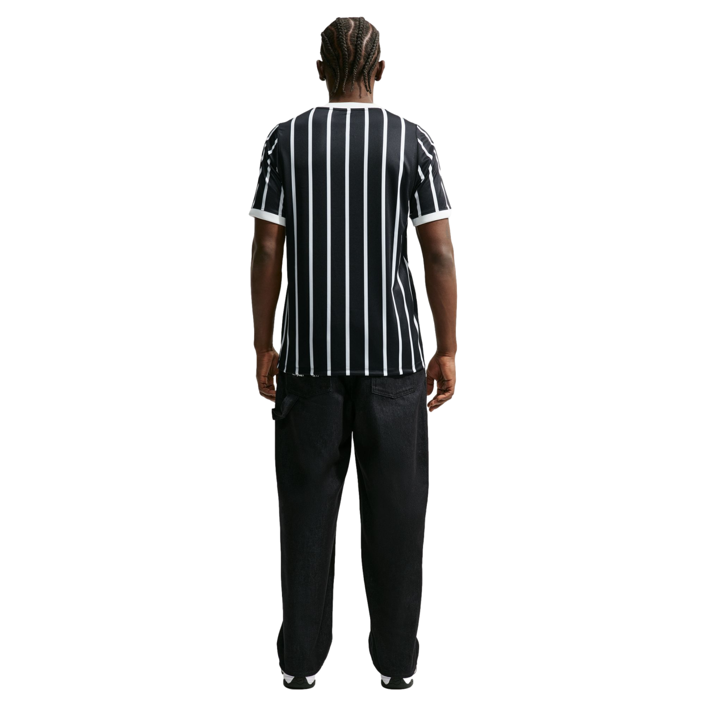 Rear view of a man with braided hair wearing a black and white vertical striped T-shirt and black trousers against a solid black background.