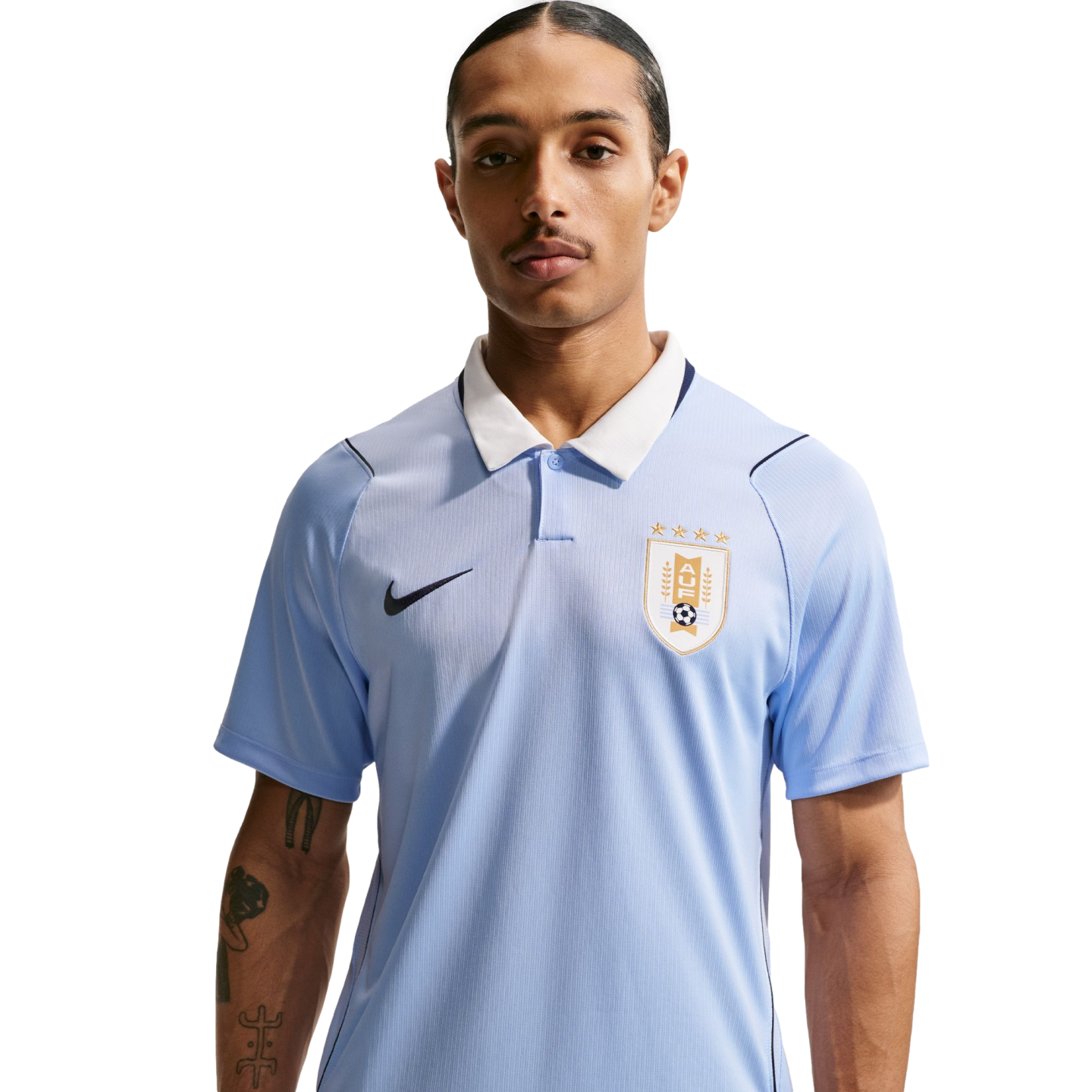 A man with a mustache wears a light blue Uruguay national football team polo shirt with a white collar and Nike logo against a black background.