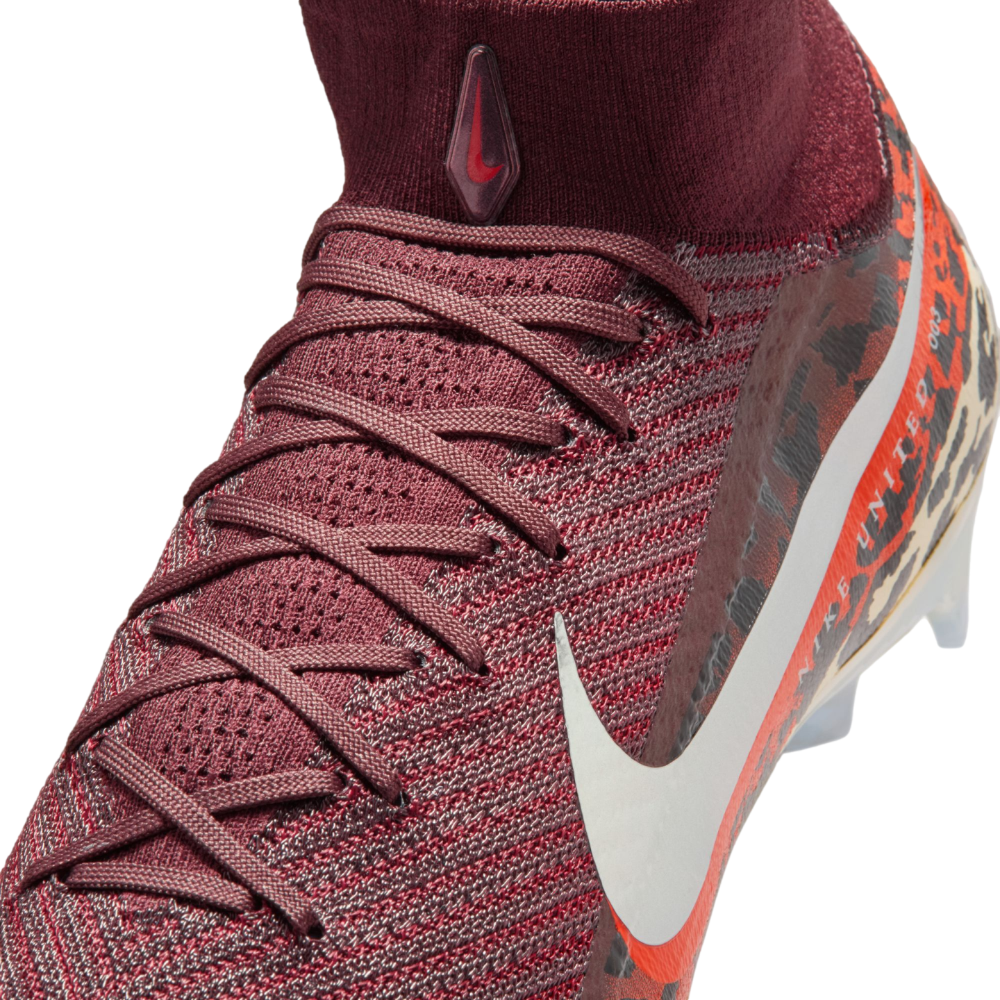 A close-up, high-angle shot shows a maroon Nike soccer cleat against a black background. The shoe features a textured, knit upper with maroon laces and a high-top sock collar. A small, teardrop-shaped logo with a red swoosh is on the front of the collar, and a large white swoosh is visible on the side over an orange and leopard print pattern that includes the text "NIKE UNITED."