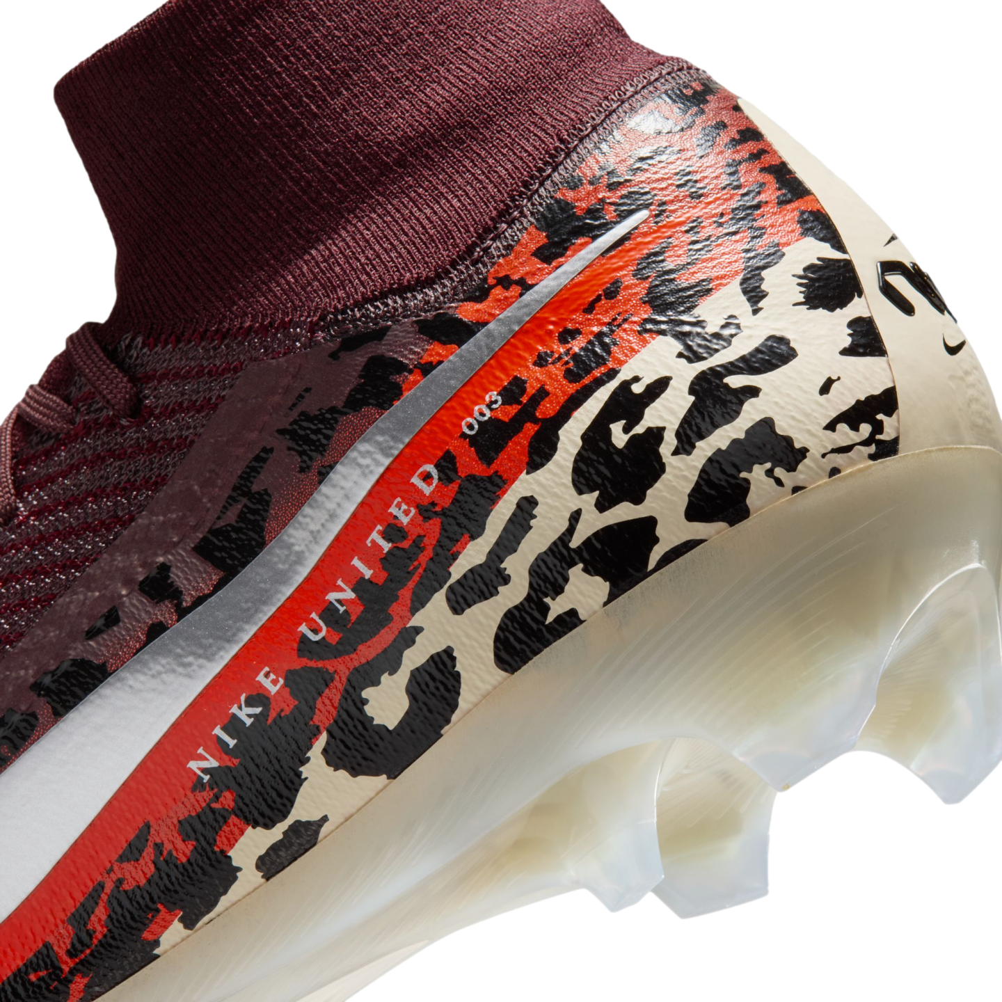 A close-up, angled view of the heel and ankle area of a Nike soccer cleat against a black background. The shoe features a burgundy ribbed knit ankle collar and a main body decorated with a bold leopard-print pattern in cream, black, and vibrant orange. A red stripe running diagonally across the side contains the text "NIKE UNITED 003" in white, positioned next to a metallic silver swoosh detail. The bottom shows a semi-translucent white soleplate with molded studs.