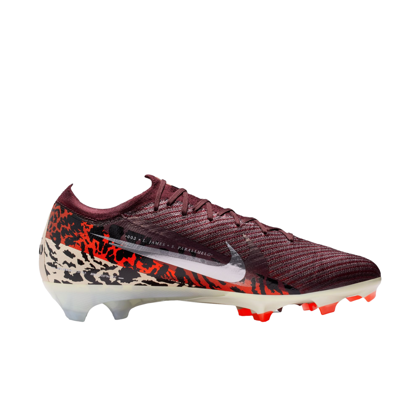 A side-profile studio shot of a Nike Mercurial soccer cleat against a solid black background. The shoe features a deep maroon ribbed upper and a large white Nike swoosh. The lower half of the boot is adorned with a bold graphic pattern in orange, black, and off-white. It is finished with an off-white soleplate and bright orange studs.