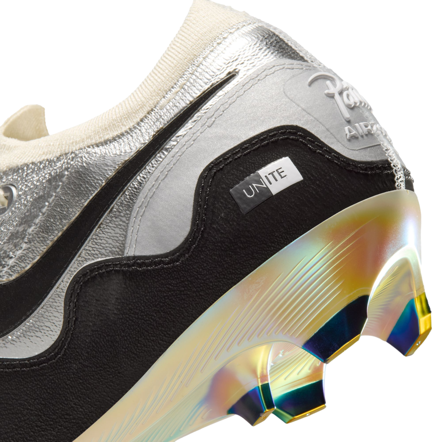Close-up of a silver and black soccer cleat's heel, featuring a small "UNITE" tag and a shimmering iridescent gold and purple sole with metallic studs.