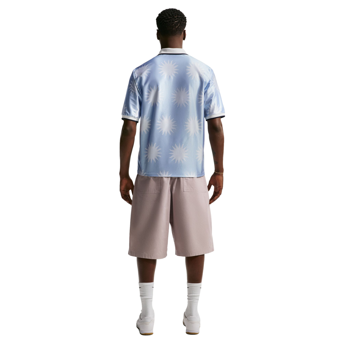 Back view of a man wearing a light blue sunburst-patterned polo shirt, mauve shorts, white socks, and white sneakers.