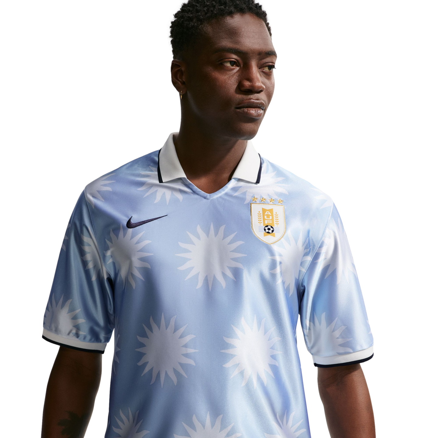 A man in a light blue Nike Uruguay football jersey with a white sun pattern and polo collar, looking to the side against a white background.