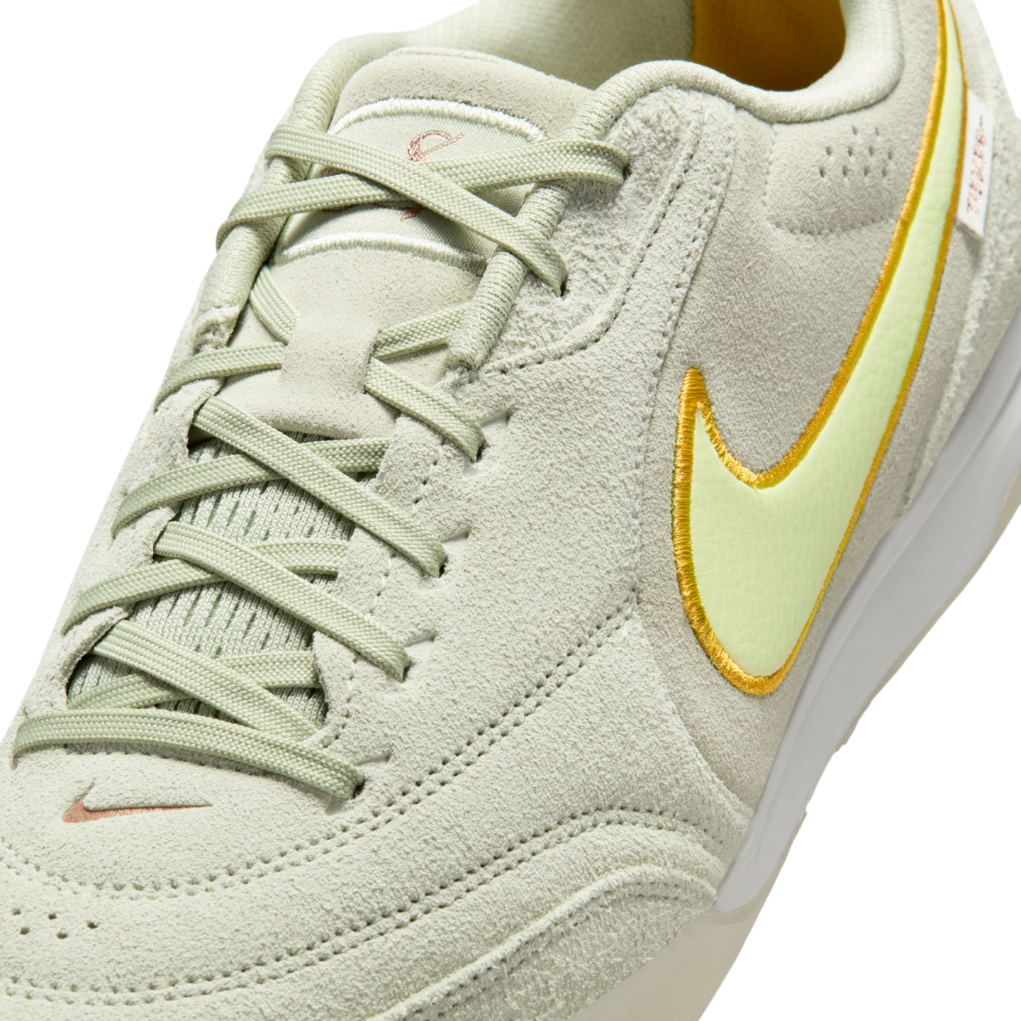 Close-up of a light green suede Nike sneaker featuring a pale yellow swoosh with a yellow border, matching laces, and a small orange swoosh embroidered near the toe.