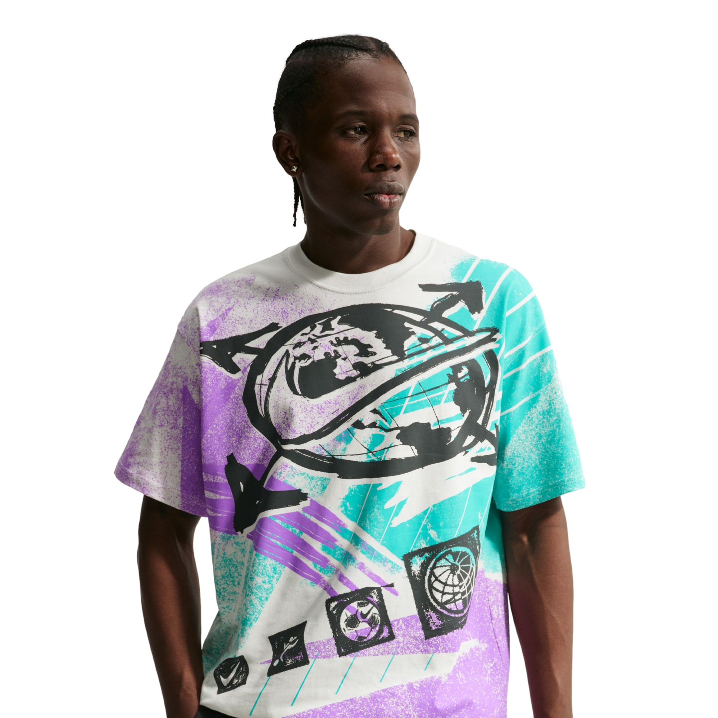 A young Black man with braided hair poses against a solid black background, wearing a white Nike t-shirt with a large, vibrant graphic. The shirt's central design features a black globe with a Nike swoosh wrapped around it, surrounded by bold, textured splashes of teal and purple paint. He is looking off to the side with a neutral expression.