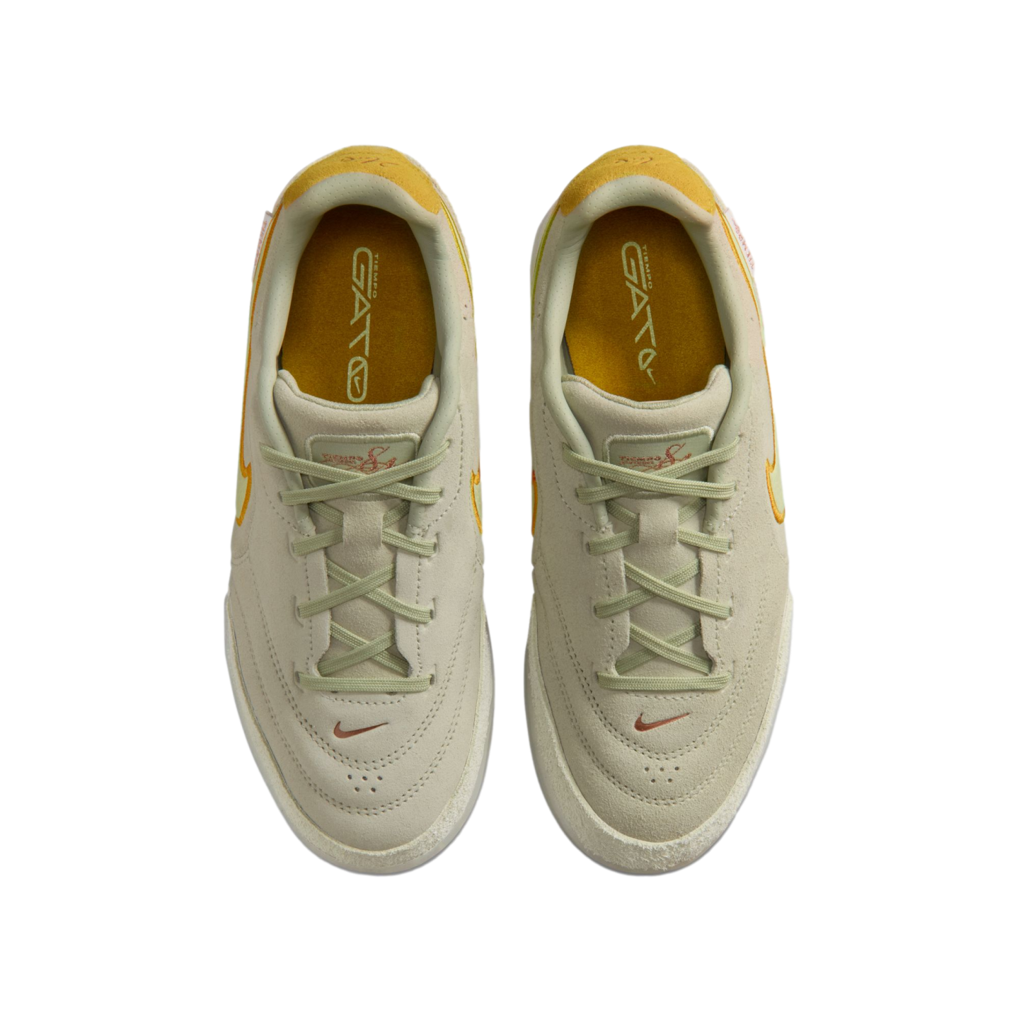 A top-down view of a pair of off-white Nike Tiempo Gato sneakers with yellow accents and beige laces on a black background.