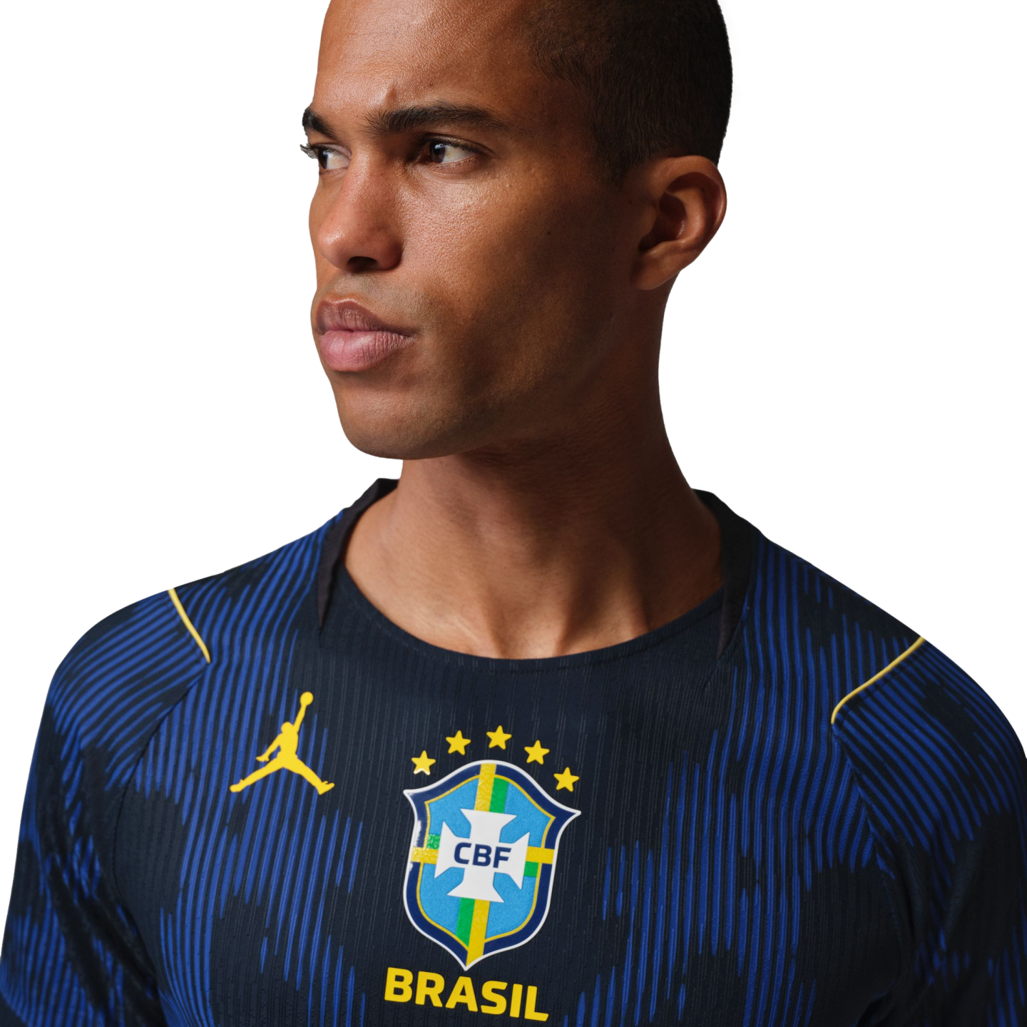 A man in a blue Brazil soccer jersey with yellow Jordan and CBF logos, looking sideways against a black background.