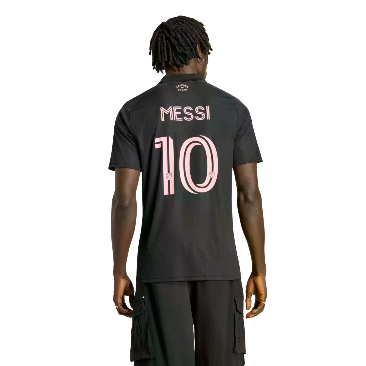Back view of a man with dreadlocks wearing a black Inter Miami CF soccer jersey with "MESSI" and number "10" in pink. He is standing against a solid black background.