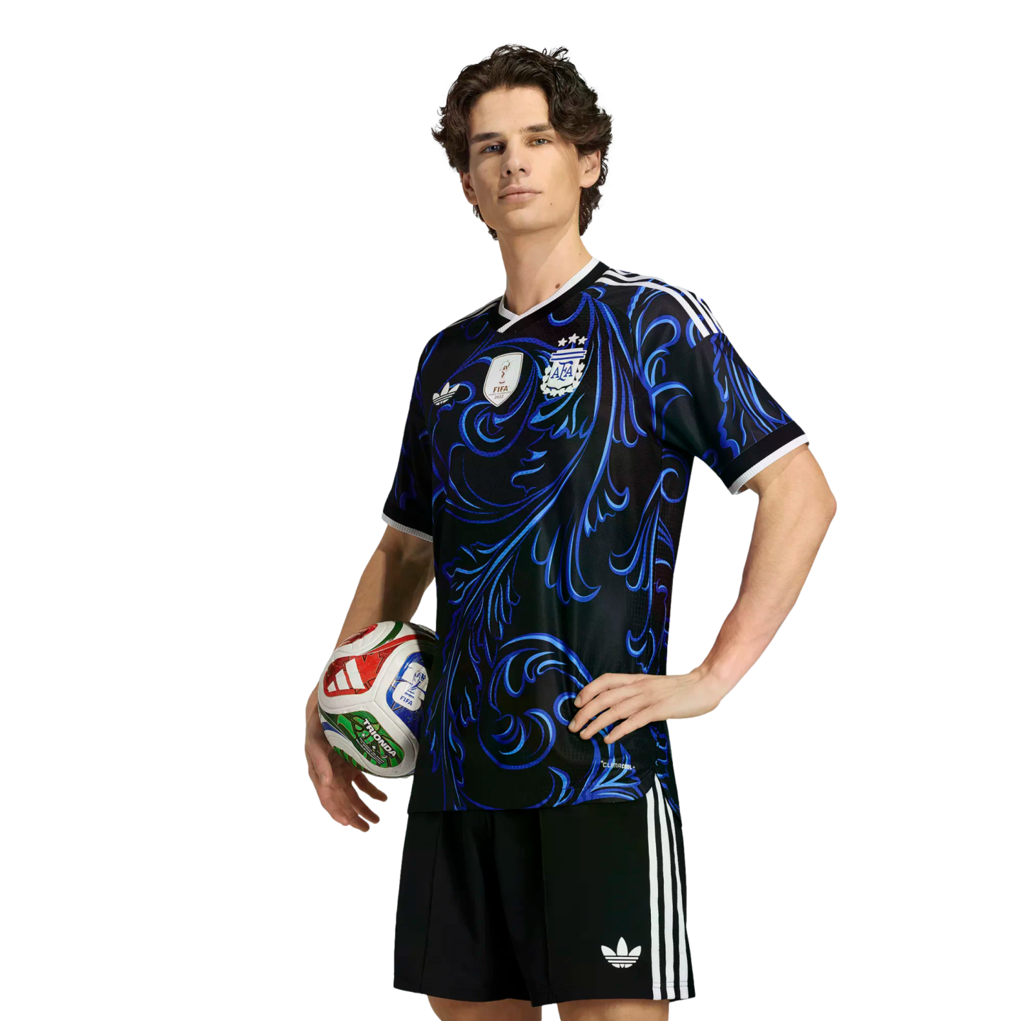 A young man models a black and blue patterned Argentina soccer jersey and shorts while holding a soccer ball against a solid black background.