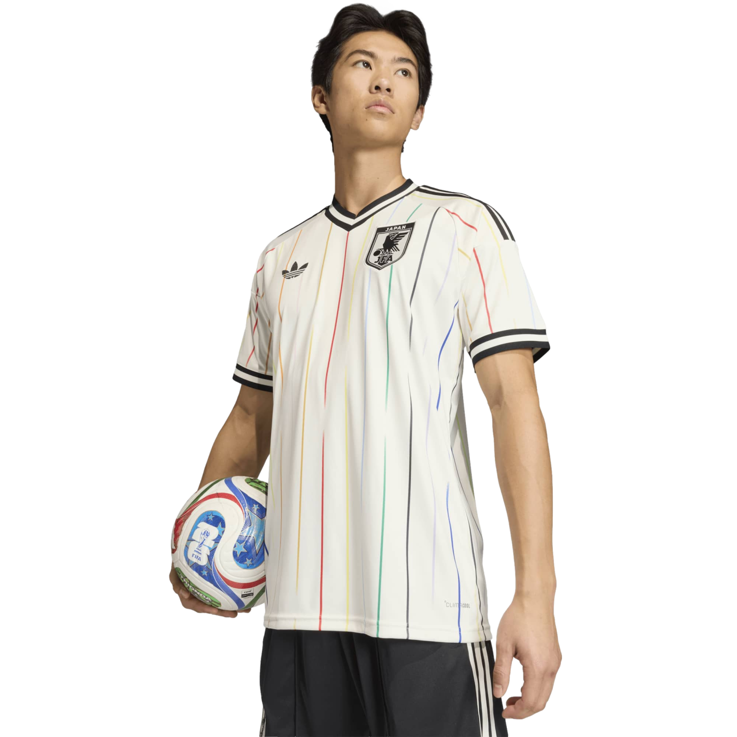 Man wearing a white Adidas Japan soccer jersey with vertical rainbow stripes, holding a colorful soccer ball against a black background.