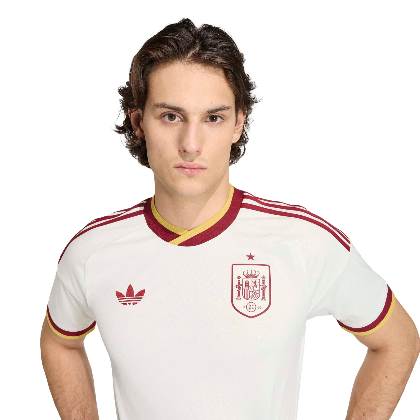 Young man with wavy brown hair in a white Spain national football team jersey with burgundy and yellow trim, against a black background.