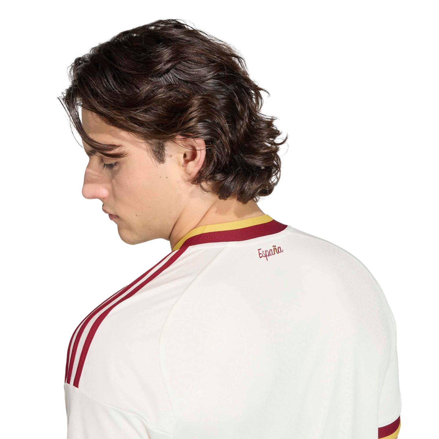 Profile of a man with wavy hair looking down, wearing a white Spanish soccer jersey with red shoulder stripes and "España" text, set against a black background.