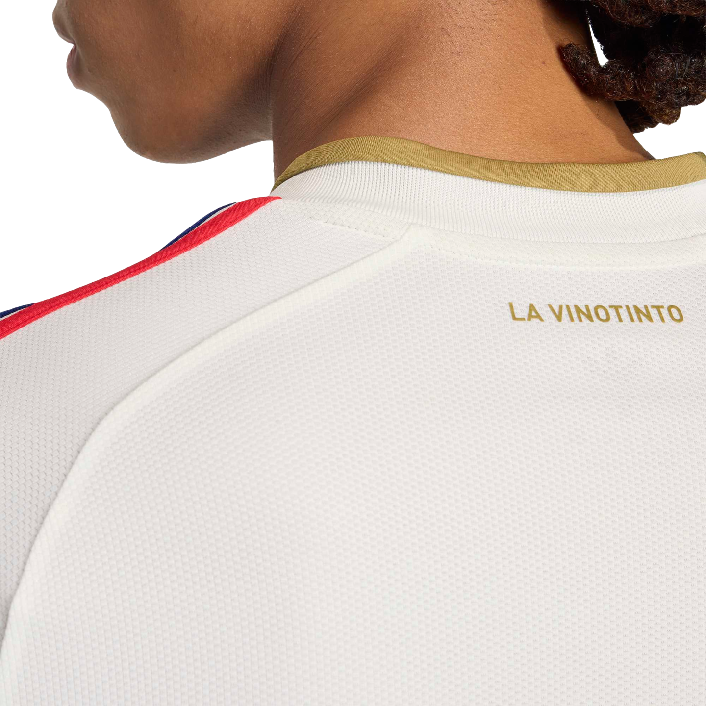 Close-up of a white mesh jersey featuring gold lettering reading "LA VINOTINTO" below a gold collar, with red and blue stripes along the shoulder.