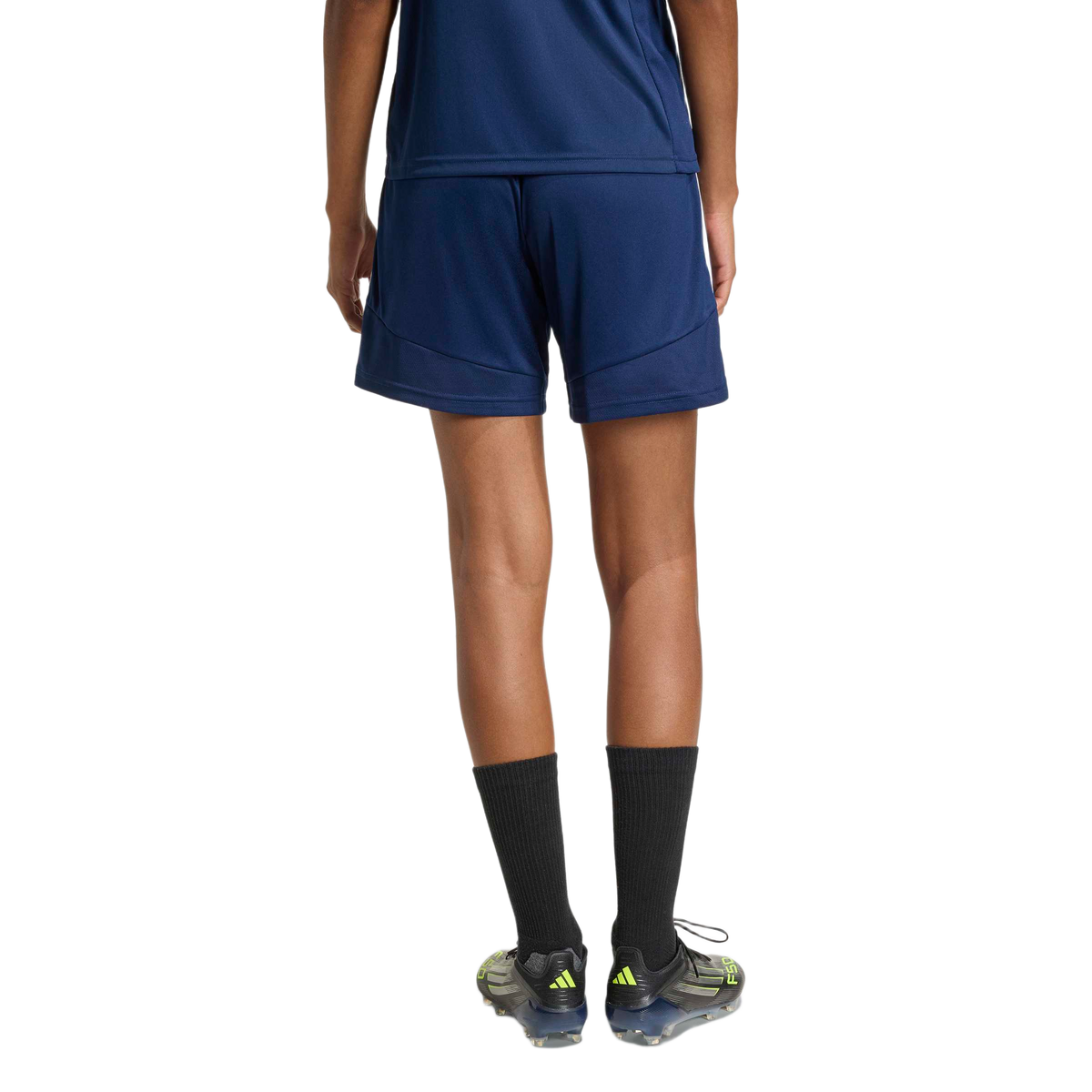 Rear view of a person wearing navy blue athletic shorts and top, tall black socks, and soccer cleats with neon yellow details.