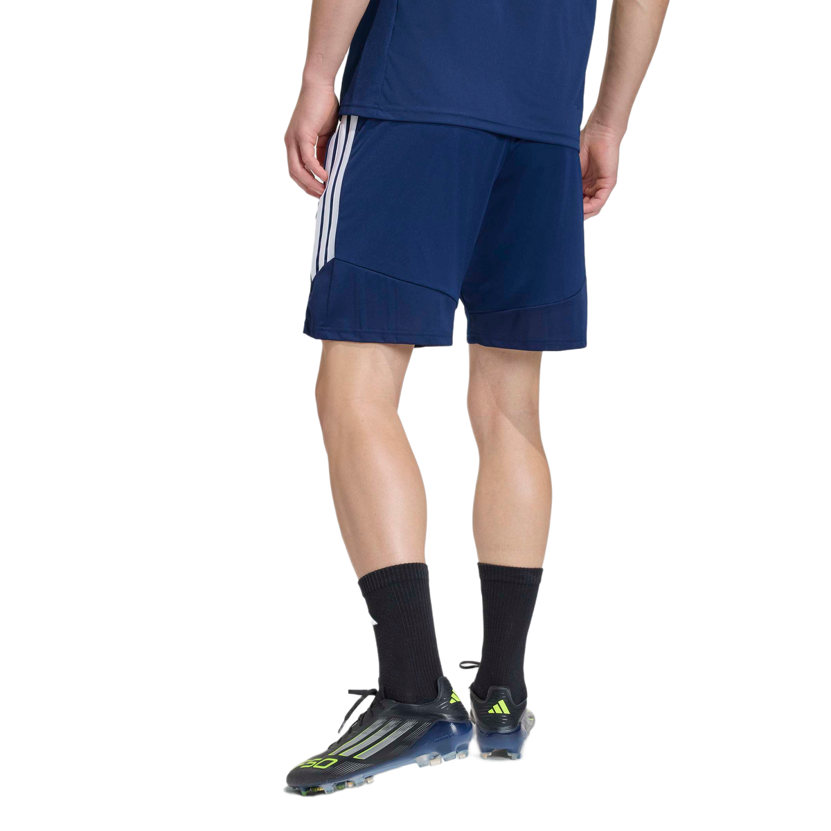 Rear view of a person from the waist down in navy shorts, black socks, and black soccer cleats with neon accents.
