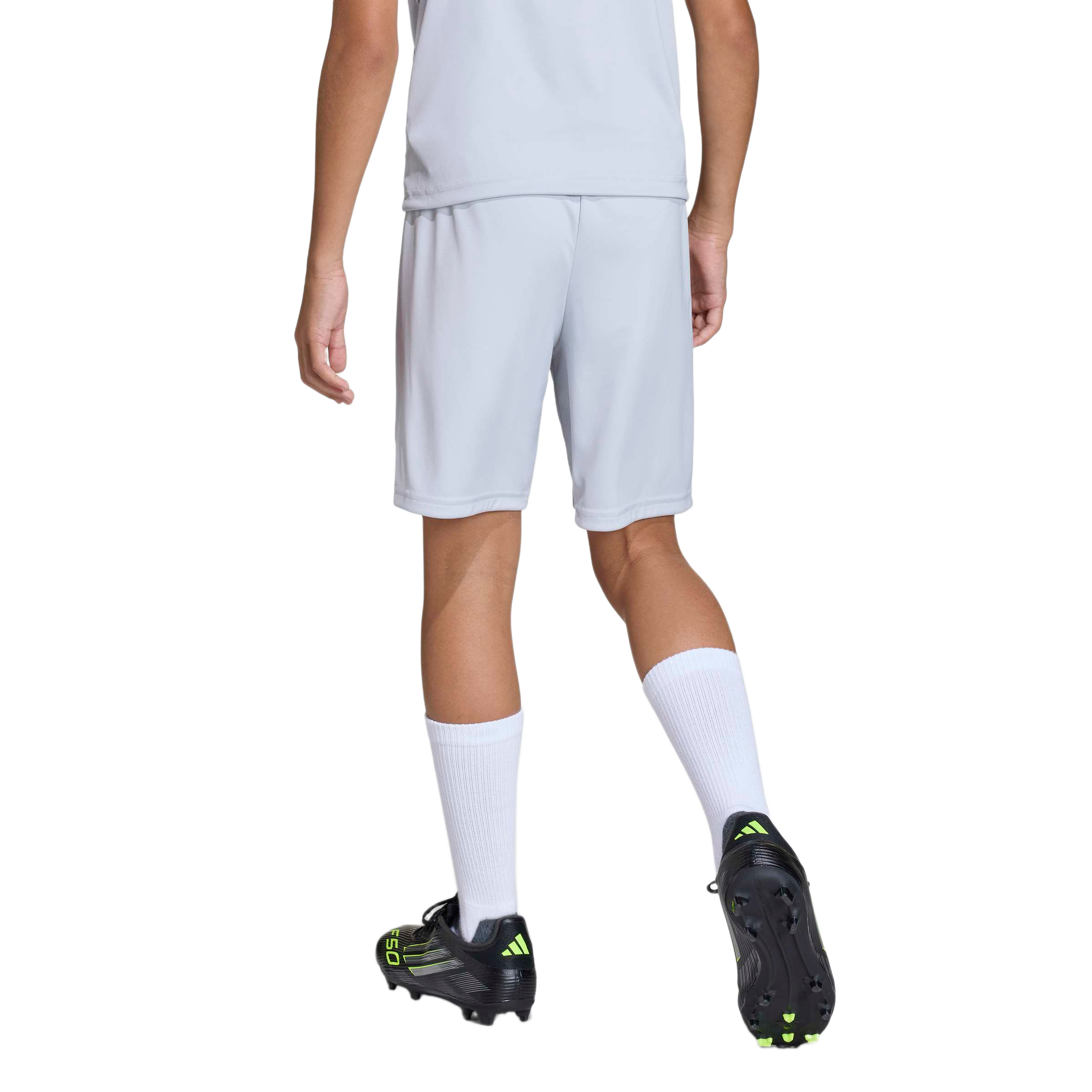Rear view of a person wearing a light gray athletic t-shirt and shorts, white crew socks, and black soccer cleats with neon yellow accents.