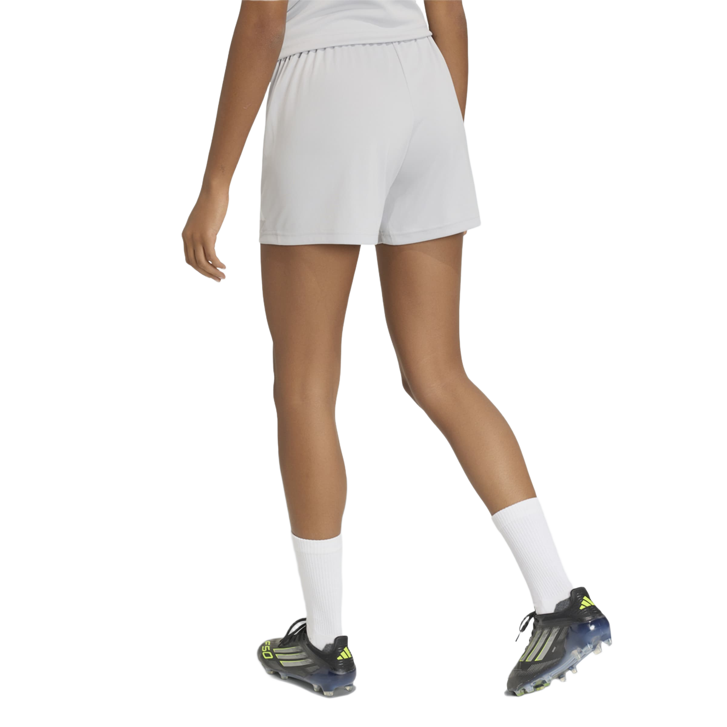 Rear view of a person wearing light grey athletic shorts, white crew socks, and black soccer cleats with neon yellow accents.