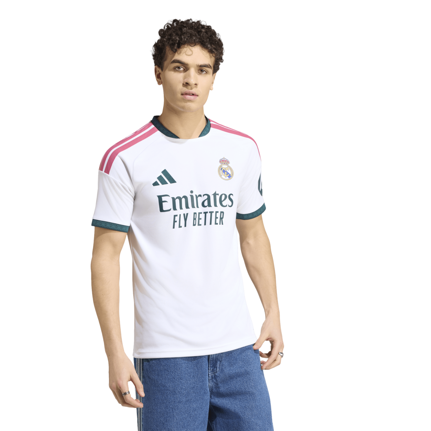A young man with curly hair modeling a white Real Madrid home jersey and blue jeans against a white background.