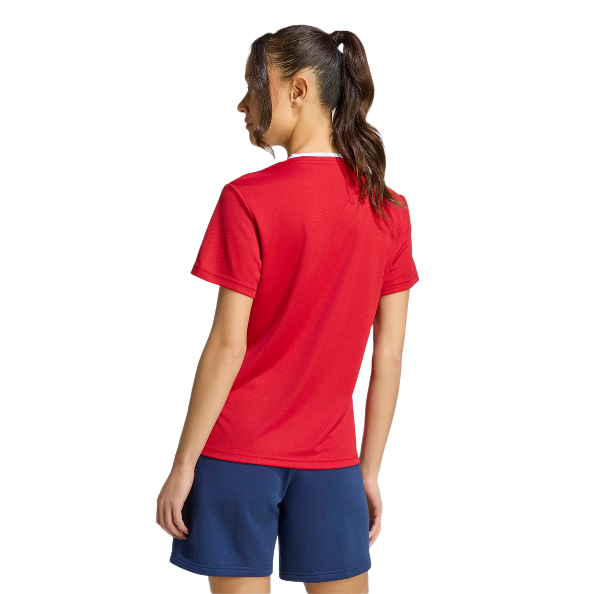 Rear view of a woman wearing a red short-sleeved athletic t-shirt and navy blue shorts against a light grey background.