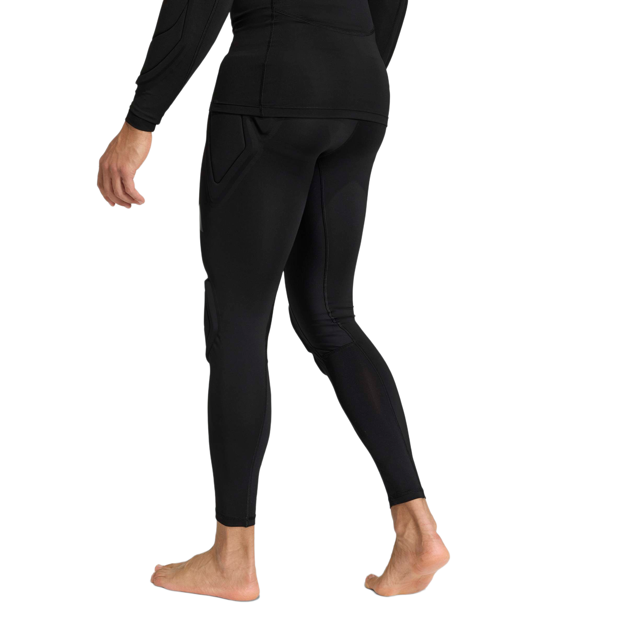 Rear view of a person wearing black padded compression leggings and a long-sleeved athletic top, standing barefoot against a plain light gray background.