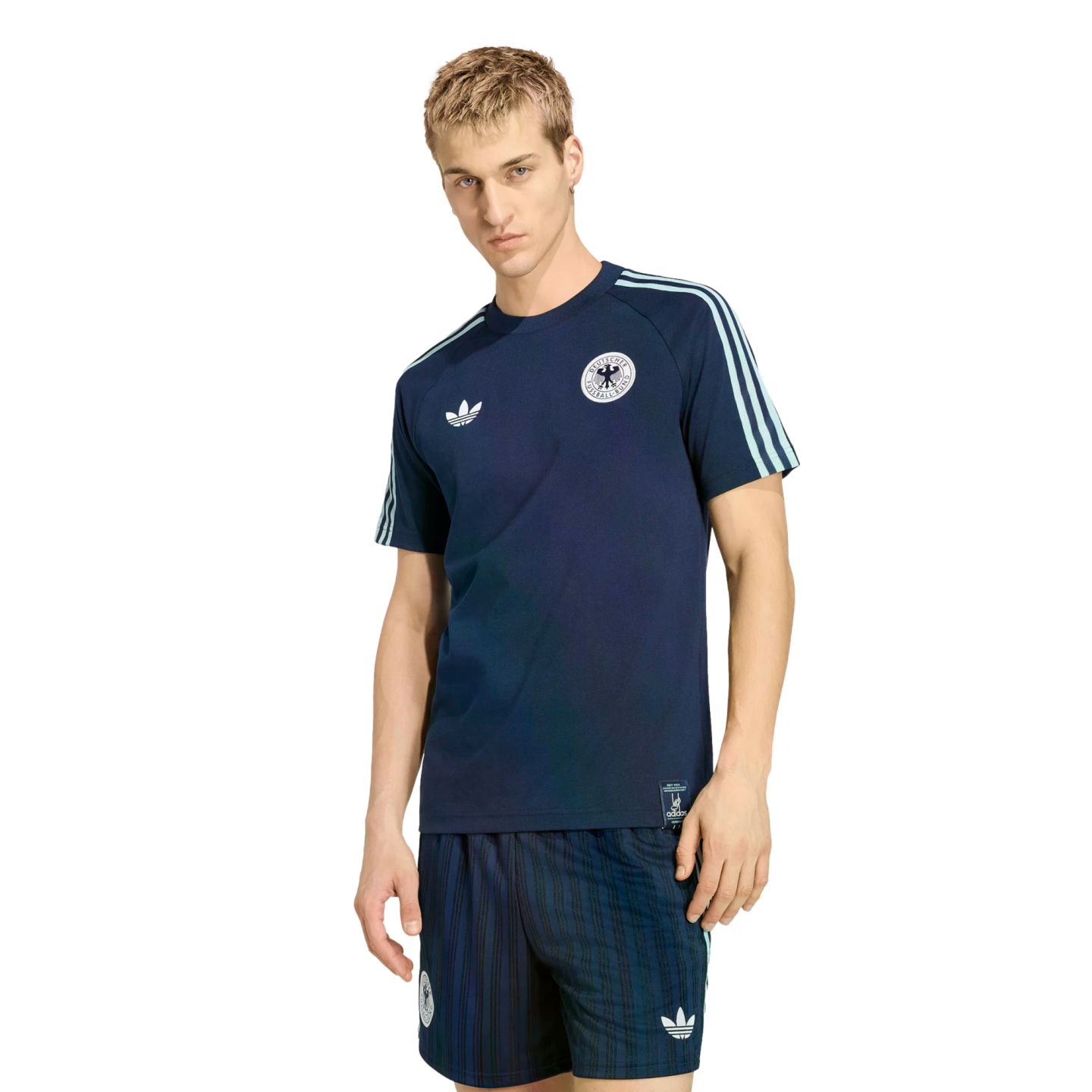 A man wearing a navy blue Adidas Germany national football team t-shirt and matching shorts, standing against a solid black background.