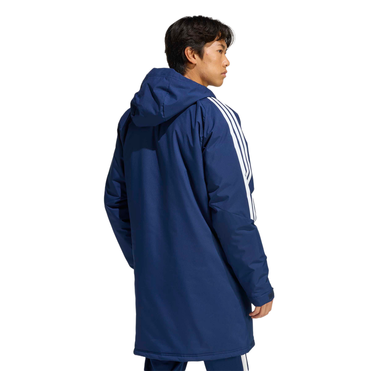 Rear three-quarter view of a man wearing a long navy blue hooded parka featuring three white stripes on the sleeves.
