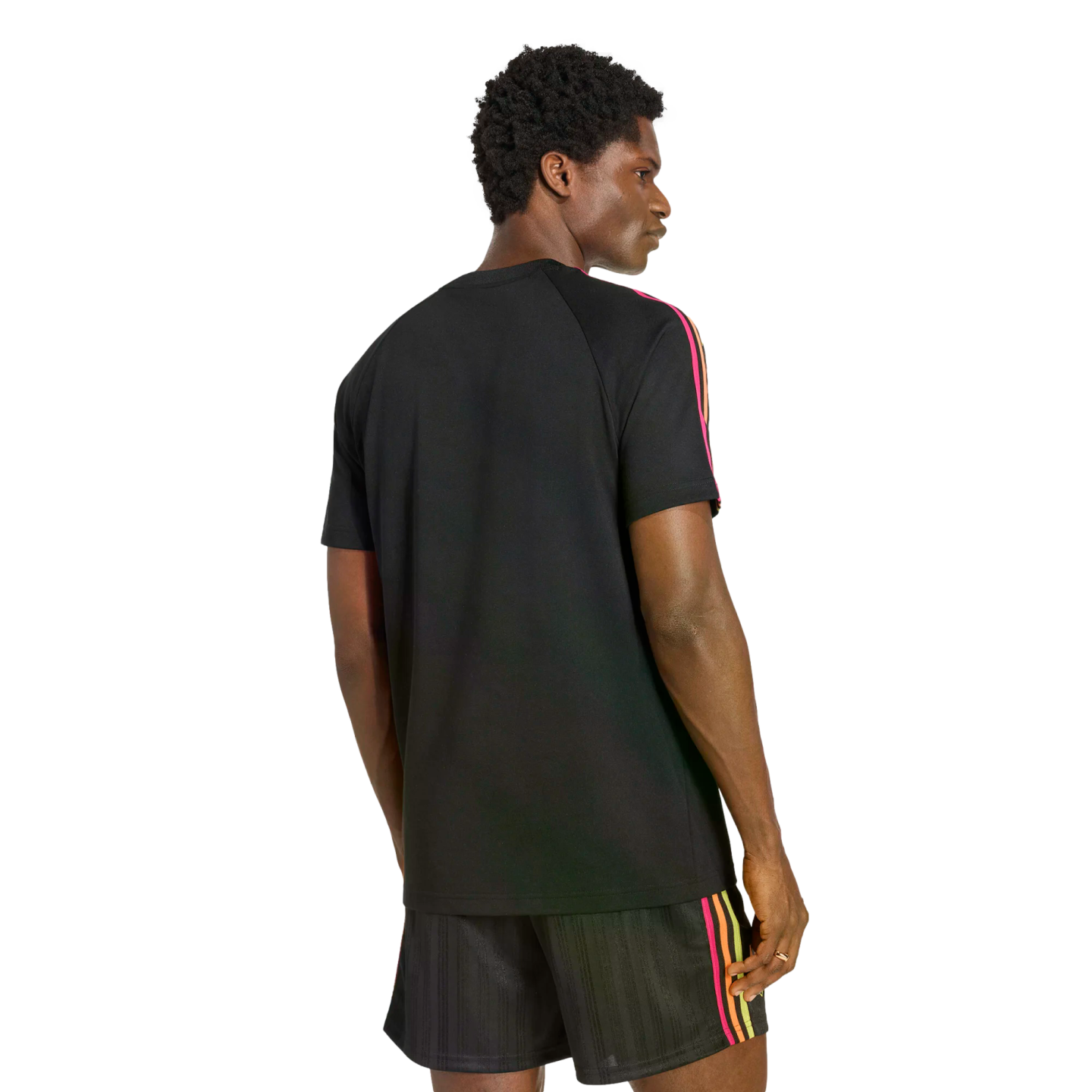 Rear view of a man looking over his shoulder, wearing a black t-shirt and matching shorts with pink, orange, and yellow stripes on the sides. He is set against a black background.