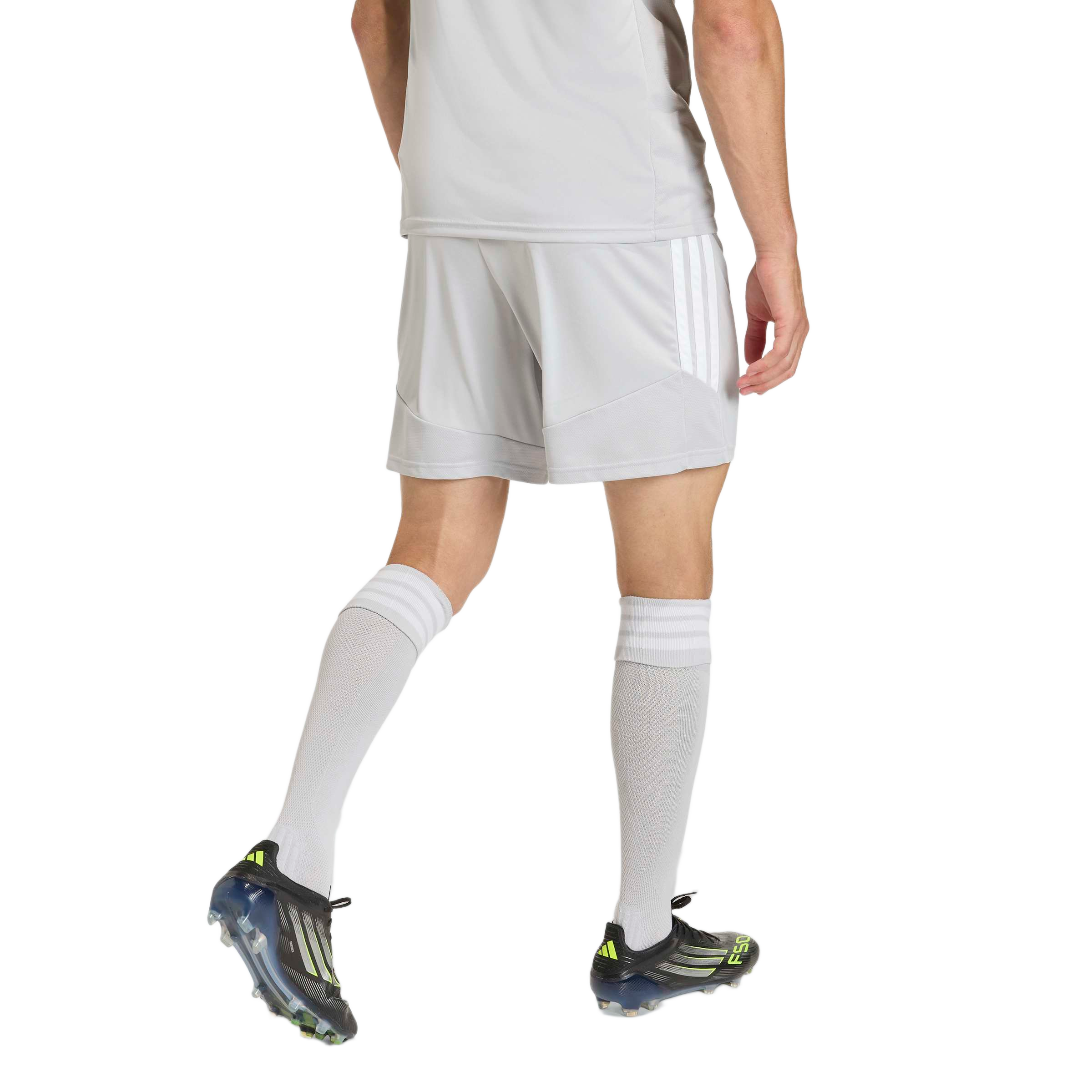Rear view of a person wearing a light grey soccer kit with white-striped shorts, tall matching socks, and black and neon green Adidas cleats.