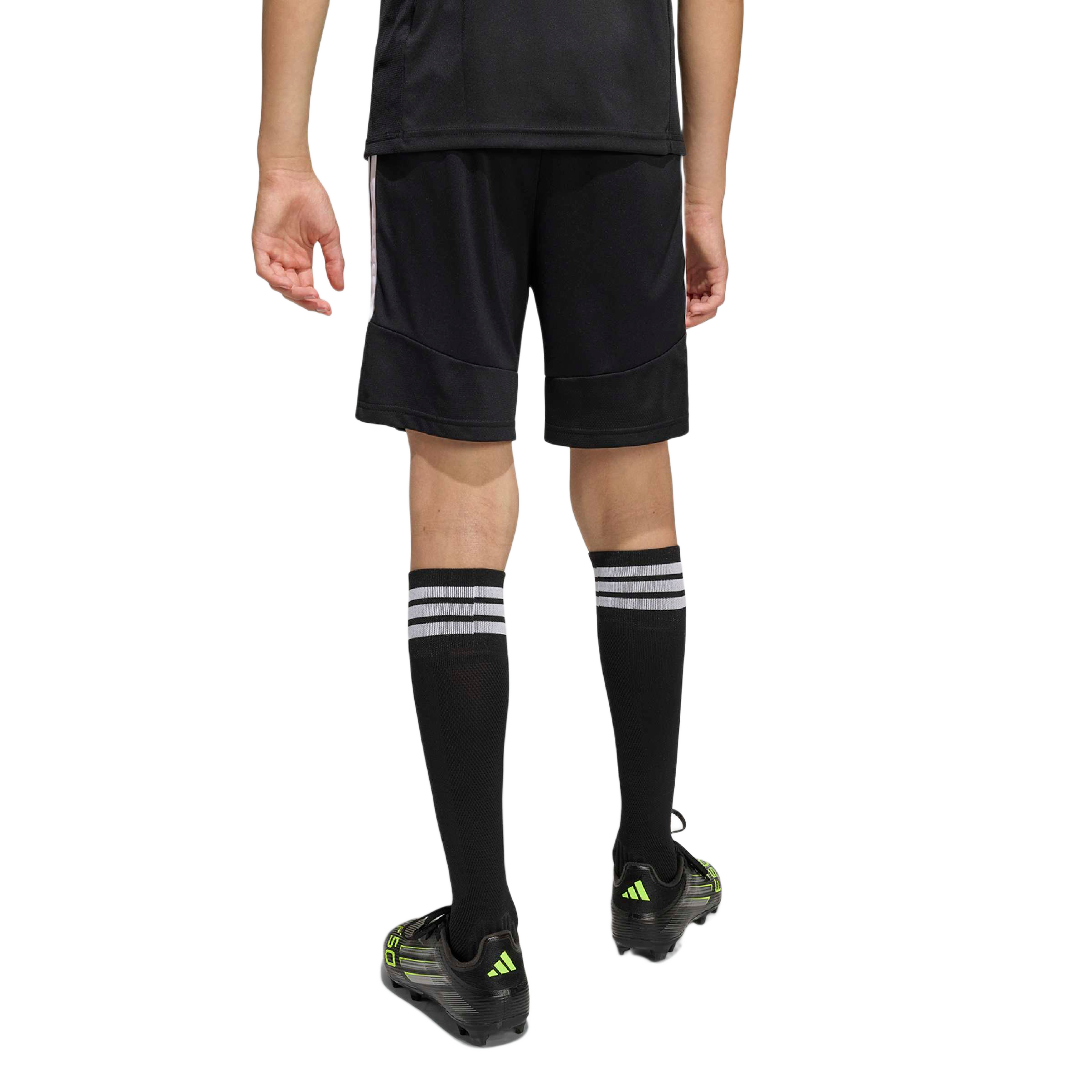 Rear view of a person in black soccer gear: jersey, shorts, tall striped socks, and black cleats with neon green accents on a light grey background.