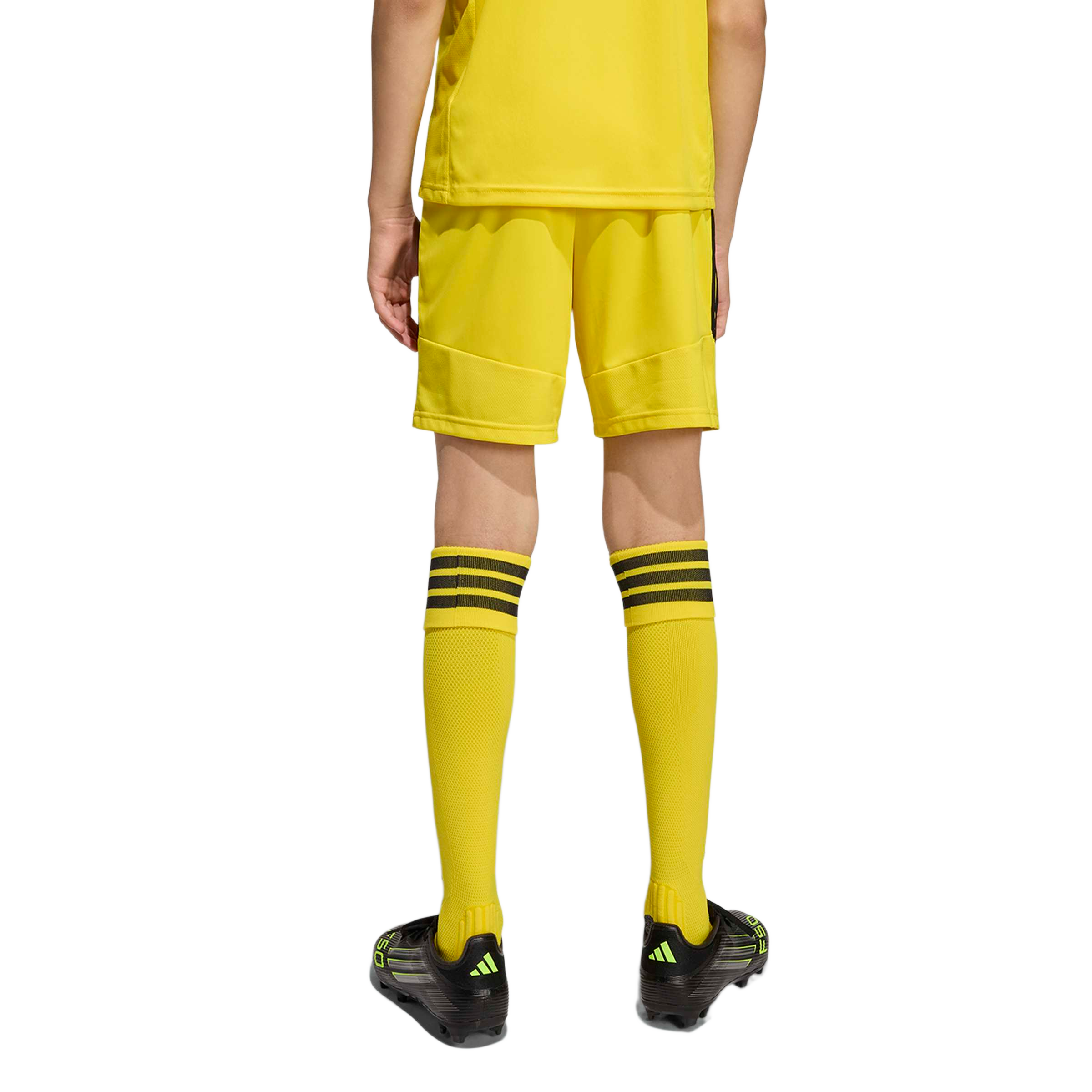 Rear view of a person wearing a yellow soccer uniform with matching socks and black cleats, standing against a light gray background.