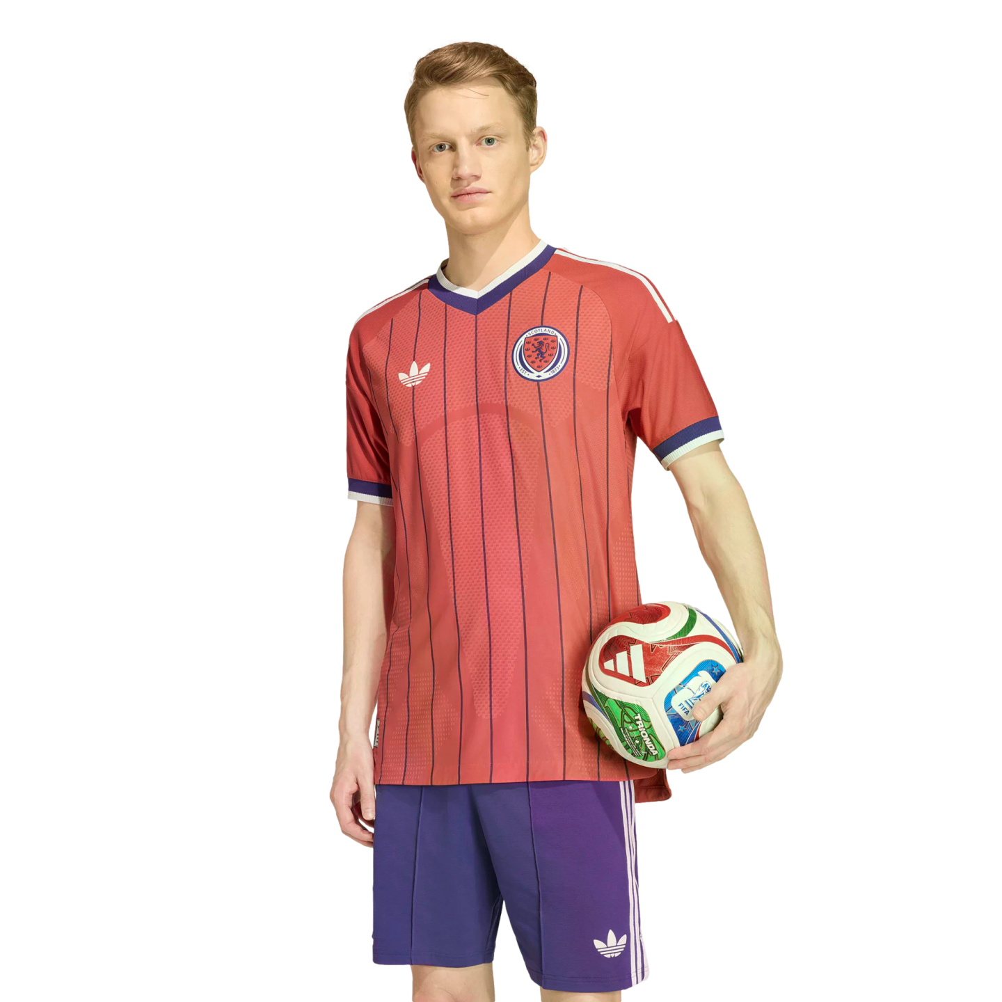 A man in a red pinstriped soccer jersey and purple shorts holds a colorful soccer ball against a white background.