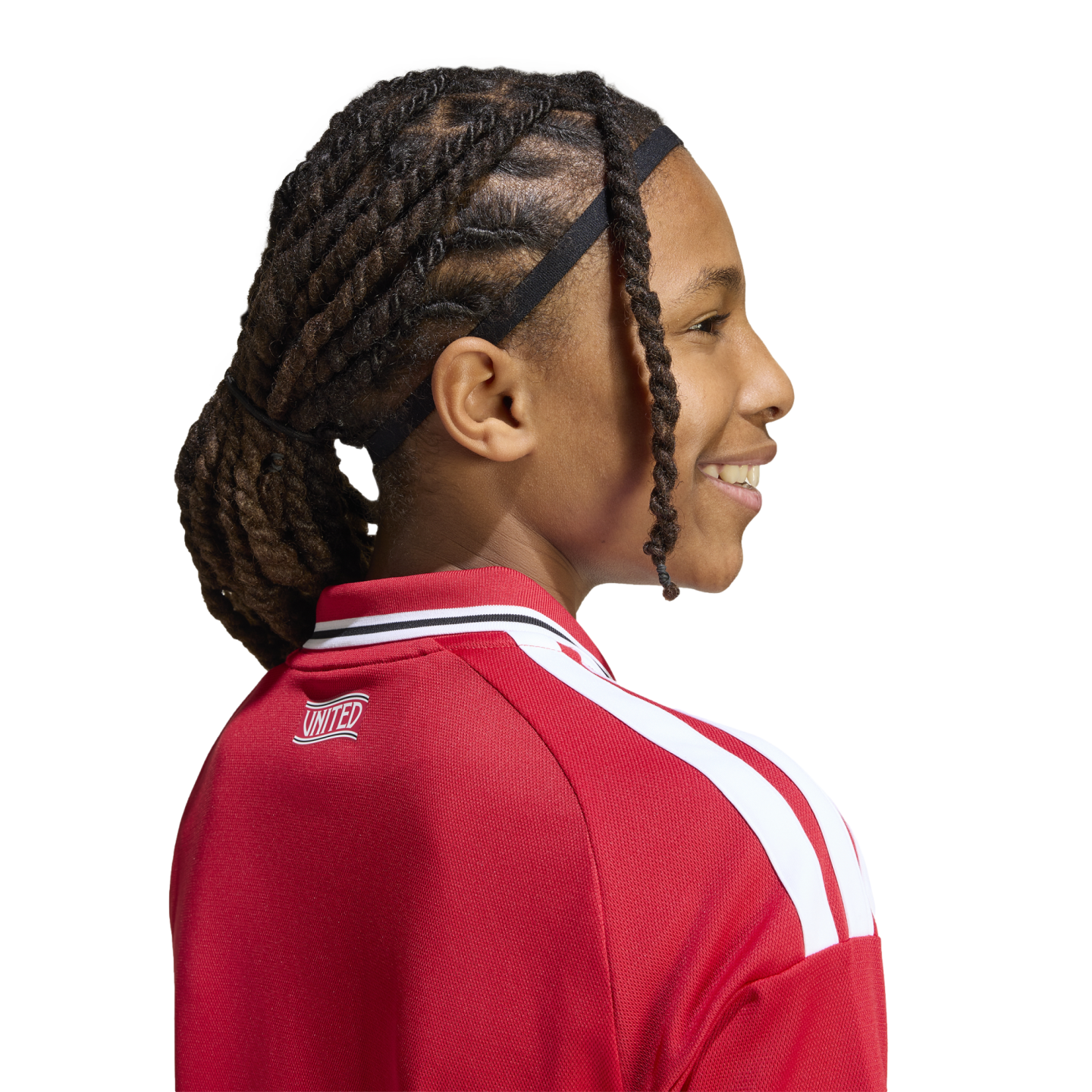 Profile of a smiling child with dark hair in twists, wearing a red and white "UNITED" athletic jacket against a white background.