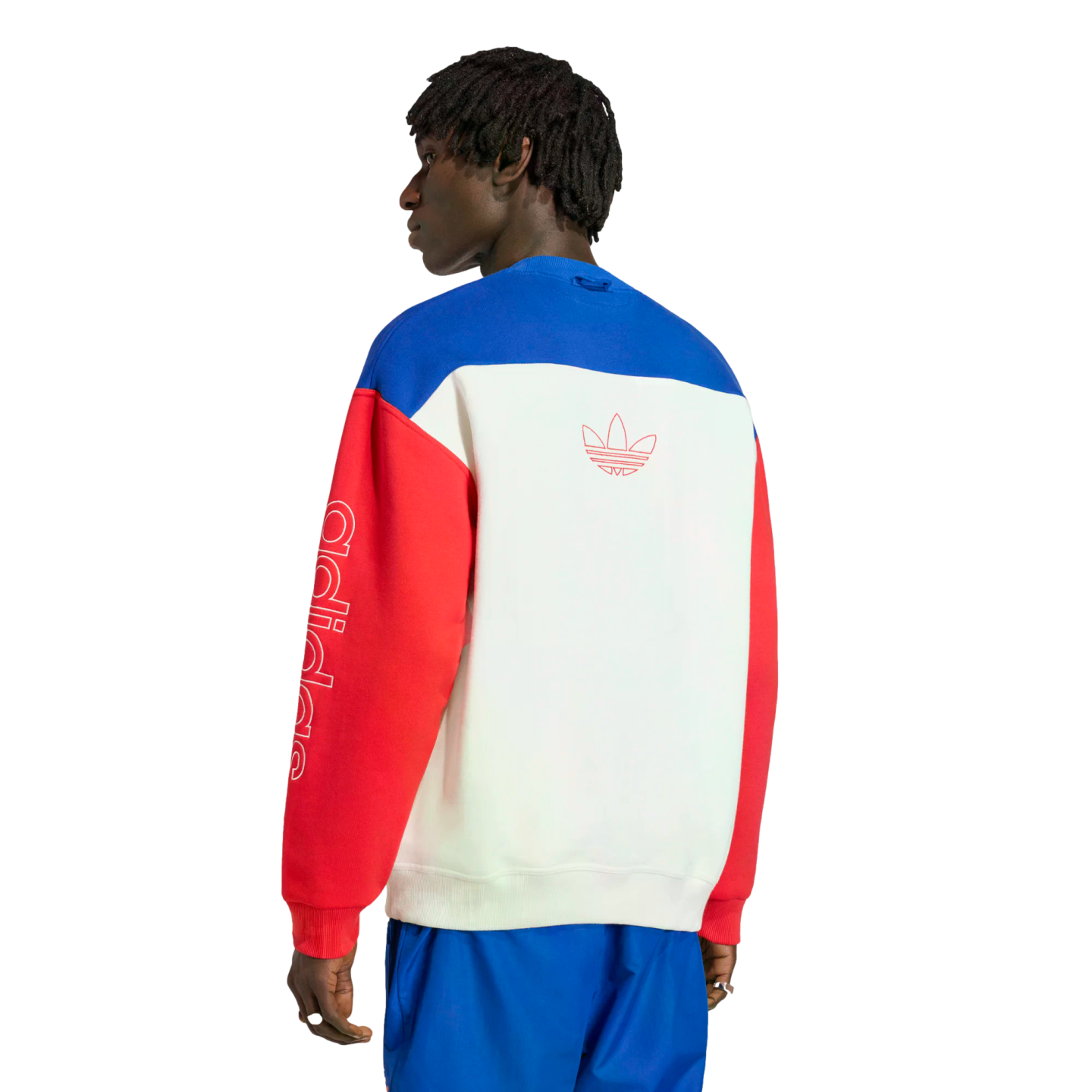A rear view of a man wearing a color-blocked Adidas crewneck sweatshirt with blue, white, and red panels. The white back panel features a red-outlined Trefoil logo, and the left red sleeve has vertical "adidas" lettering in white. He is standing against a solid black background.
