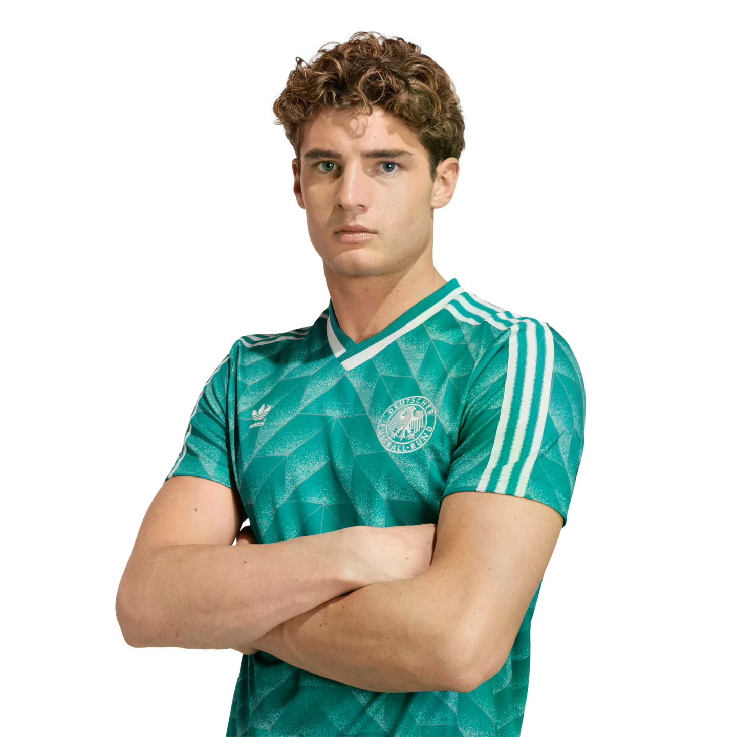 Young man with curly brown hair in a green Germany soccer jersey, posing with arms crossed against a white background.