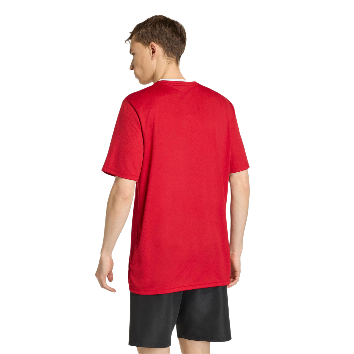 Rear view of a person wearing a bright red short-sleeved t-shirt and black athletic shorts, standing against a light gray background.