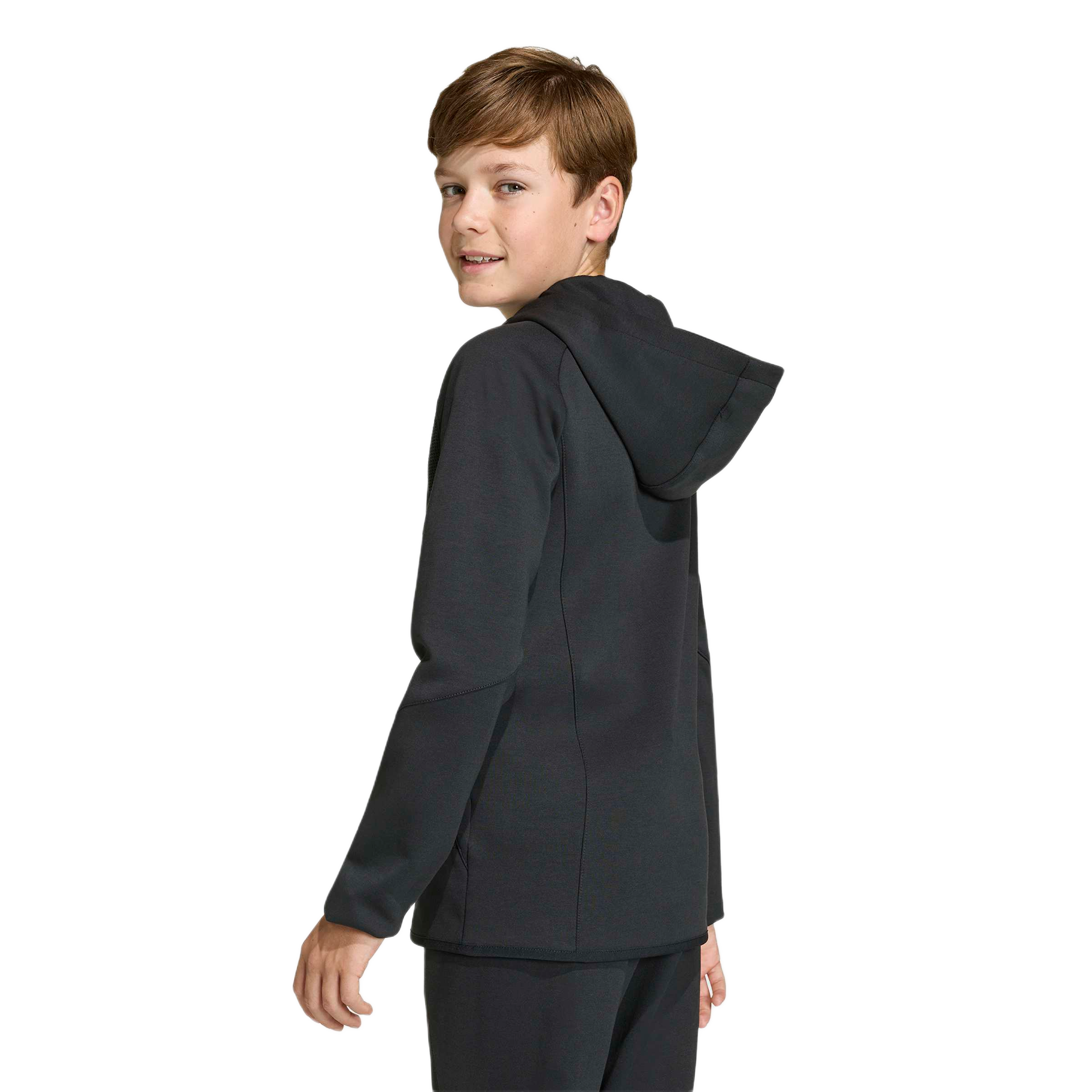A young boy looks back over his shoulder, wearing a black zip-up hoodie and matching pants against a light blue background.