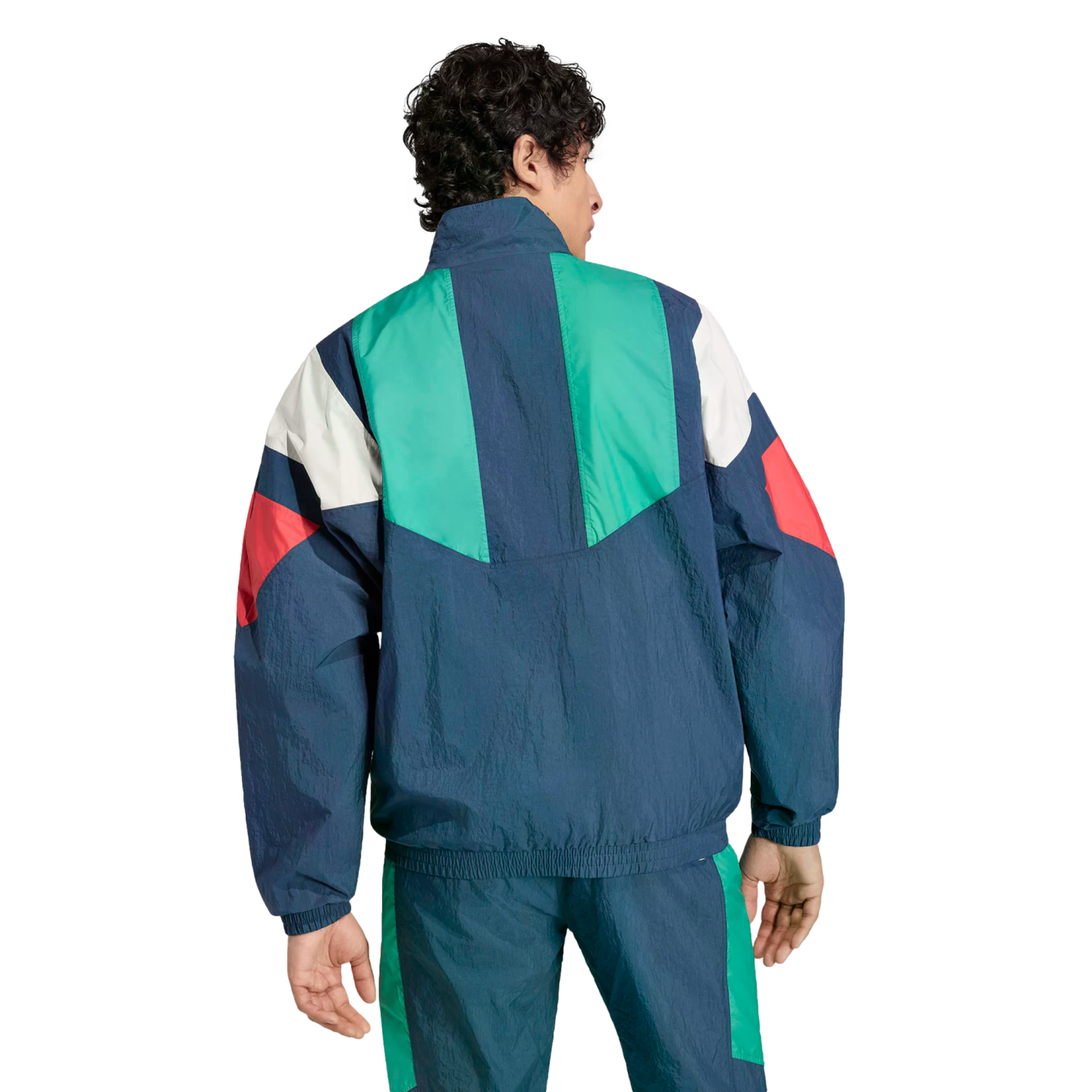 Rear view of a man wearing a retro-style, color-blocked tracksuit in navy blue, green, white, and red.